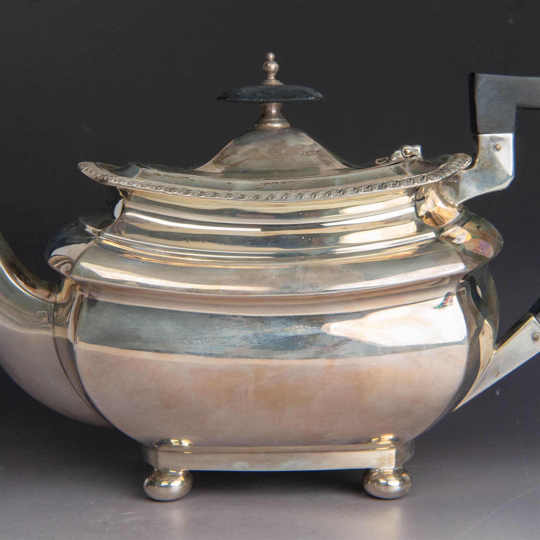 Early 20th century three piece silver tea service, comprising teapot, open sucrier and milk jug, all with oblique gadrooned rim, engraved initial to body and upon four bun feet, the teapot with Bakelite type handle and finial, hallmarked Walker & Hall, Sheffield 1912, contained within an oak presentation case with silk lining
