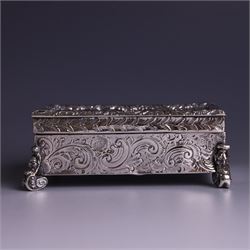 Victorian silver tobacco box, rectangular form, hinged lid embossed with a gaming scene, the body engraved with scrolls and flowers, upon four scrolling mask feet, hallmarked George Heath London 1885, H4.5cm, W10.5cm