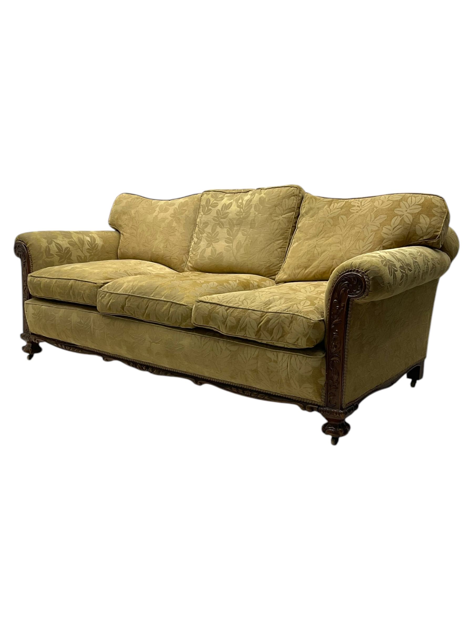 Early 20th century mahogany framed three-piece lounge suite - three-seat camelback sofa (W203cm, D105cm); pair of matching armchairs (W95cm, D96cm); upholstered in neutral foliate pattern fabric, carved with trailing leafy branches, ball and claw carved feet with brass castors 
