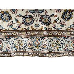 Persian Kashan ivory ground carpet, the field decorated with scrolling branches with foliate and palmette motifs, repeating border with stylised plant motifs, within floral and geometric pattern guard stripes 