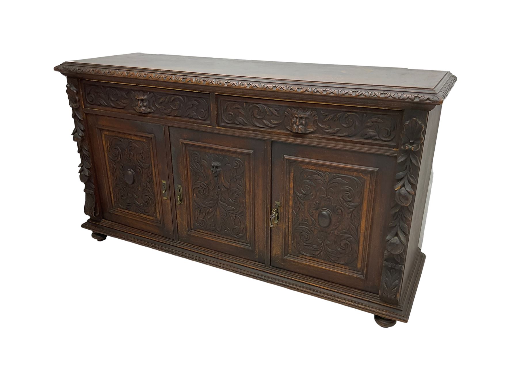 Victorian heavily carved oak sideboard, the moulded top carved with foliate decoration to the edge, fitted with two drawers and three cupboards, the drawer fronts carved with green man mask handles and scrolling foliage, the panelled doors carved with interlacing foliage, on turned compressed bun feet