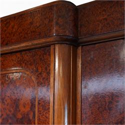 Early 20th century French burr maple breakfront armoire, enclosed by three panelled doors with bookmatched veneer and stringing, outer doors inlaid with gilt urn medallions, fitted interior with hanging spaces flanking a shelved compartment, raised on short tapered legs