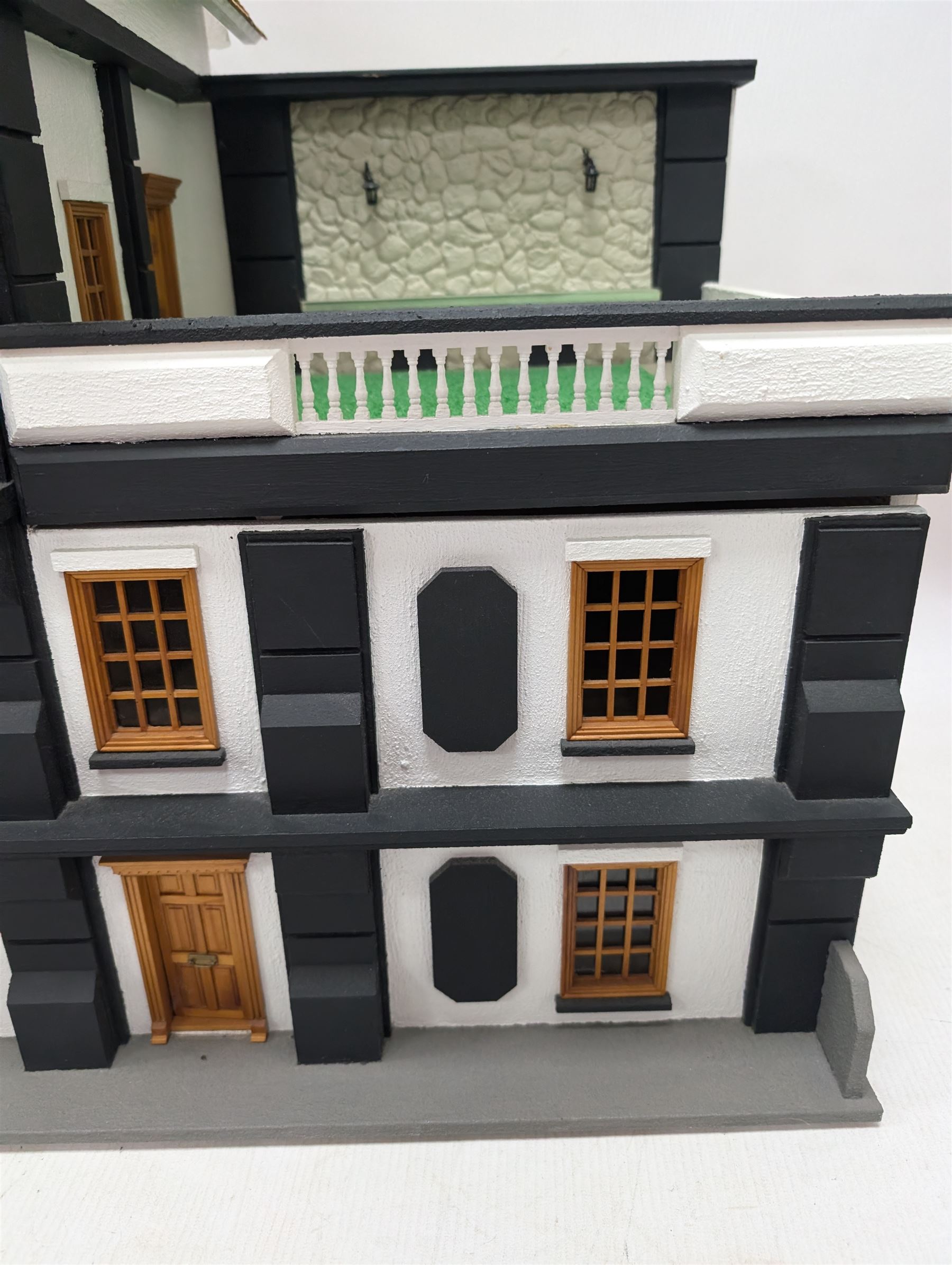 1:24 scale four-storey tudor-style dolls house, with black and white exterior, balcony garden, glazed panelled windows and wooden shingle roof, with decorated interior and wired fireplaces and lighting, H65cm, W58cm, D31cm, 