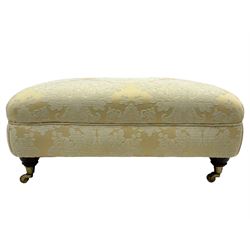 Rectangular hardwood-framed footstool, upholstered in pale gold and cream damask fabric with repeating foliate pattern, on turned feet with brass cups and castors