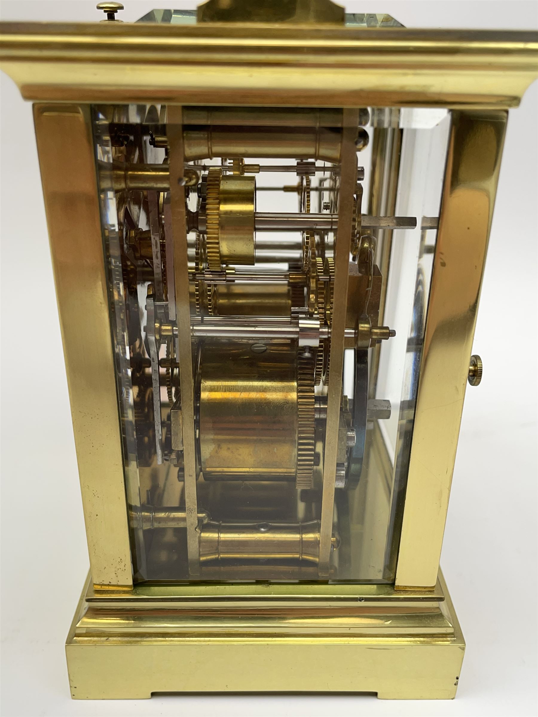 Early 20th century brass and bevelled glass repeater carriage clock with alarm, the angular and cylindrical ribbed handle and repeater button over stepped cavetto cornice, white enamel Roman dial with Arabic subsidiary alarm set dial, twin train eight day movement striking the hours and half on coil, separate alarm mechanism train, stepped moulded and plain faced base, with leather travelling case