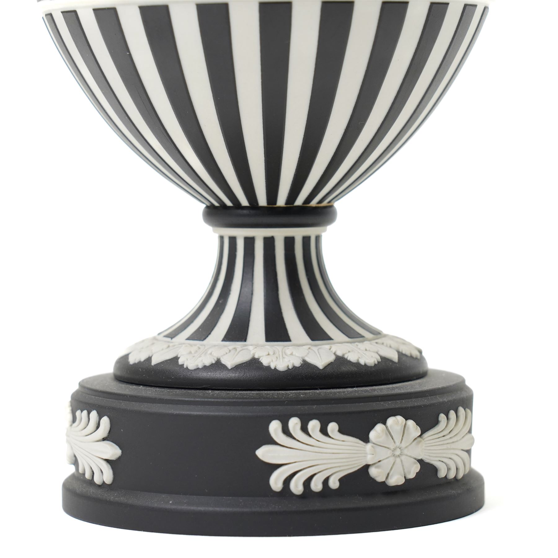 Wedgwood 20th century 'Dancing Hours' jasperware urn, the upper section decorated with a single band of neoclassical maidens in white to a black basalt ground, rising from a circular plinth decorated with foliate motifs, complete with cover with acorn finial, stamped 'Wedgwood Made in England', H25cm 