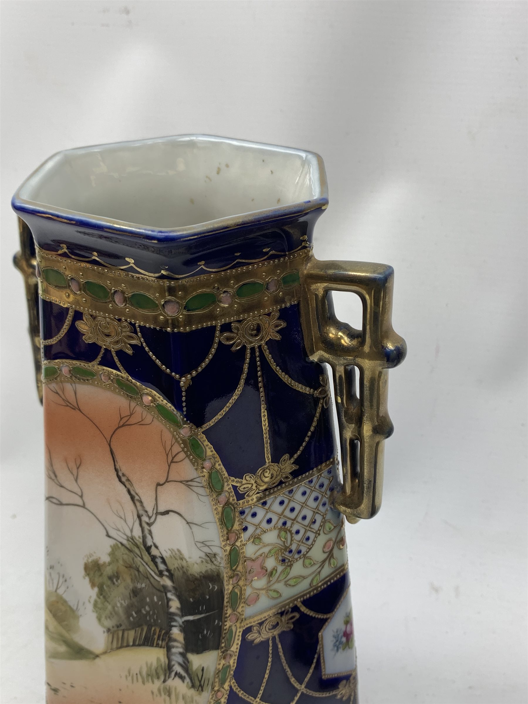 A pair of Japanese Nippon Kinjo vases, of tapering hexagonal form with twin stylised handles, the cobalt blue ground with oval hand painted panels to front and verso depicting landscapes, further detailed with smaller floral bands and panels and heightened with gilt, each with mark beneath, H30.5cm.  