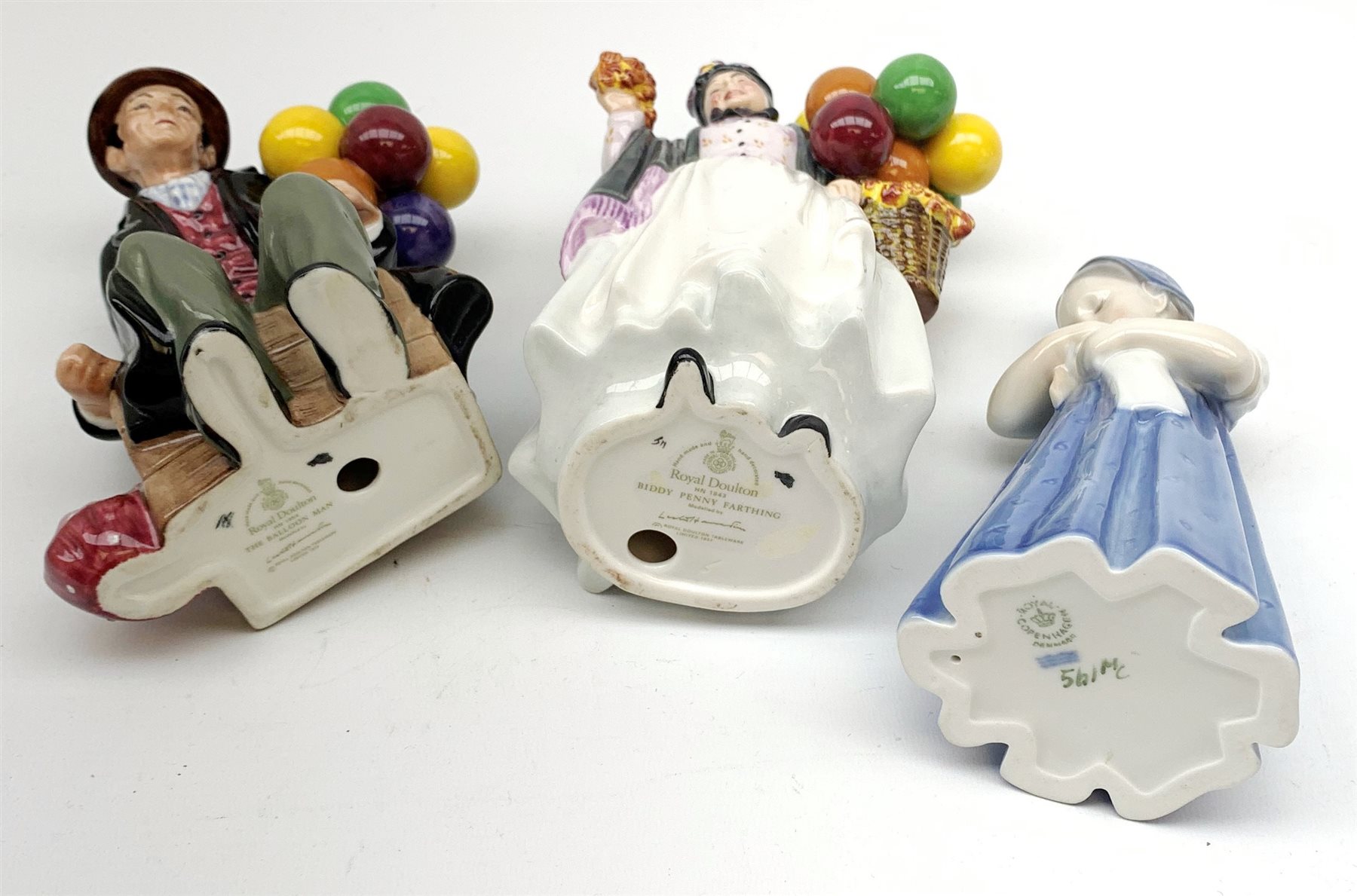 Royal Copenhagen figure of a young girl holding a doll and two Royal Doulton figures: Biddy Penny Farthing and The Balloon Man (3)