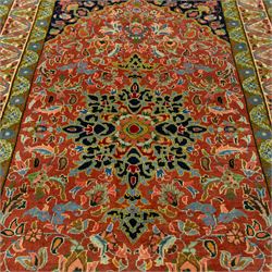 South Persian Sirjan hand-knotted carpet, terracotta ground, with a central shaped dark navy floral medallion with pendants, surrounded by scrolling foliate and floral motifs incorporating palmettes, rosettes and stylised vine work in blue, green and ivory tones, enclosed by dark navy spandrels and a wide green and ivory border with repeating palmettes and angular leaf motifs, flanked by patterned guard stripes, with cotton fringes