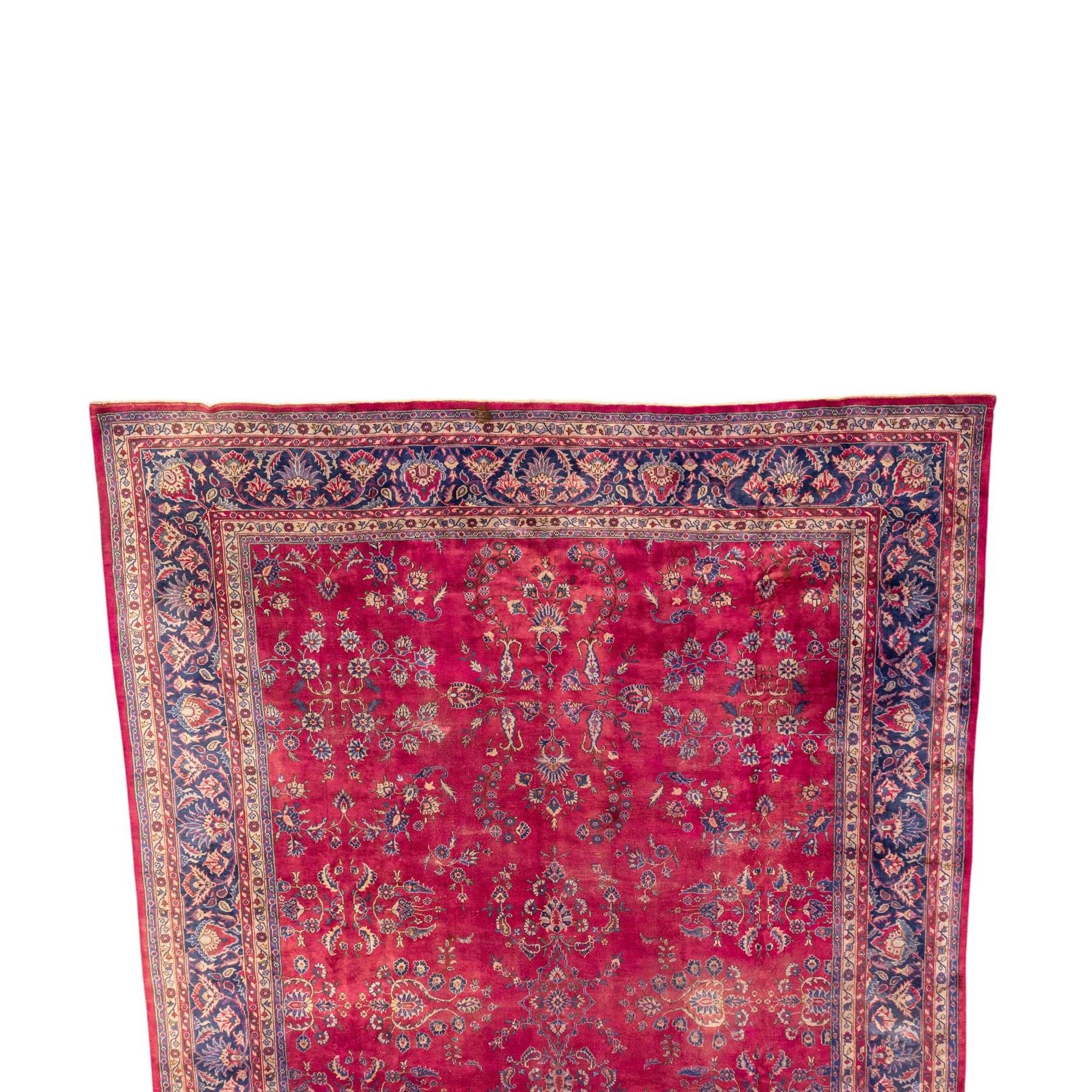 Large Persian-style mahal-type hand-knotted carpet, of rectangular form with a deep crimson field decorated with an all-over arrangement of stylized floral sprays and palmettes, with a central subtle medallion composition enclosed by a dark navy main border of scrolling floral motifs between narrow guard stripes with fringe ends 