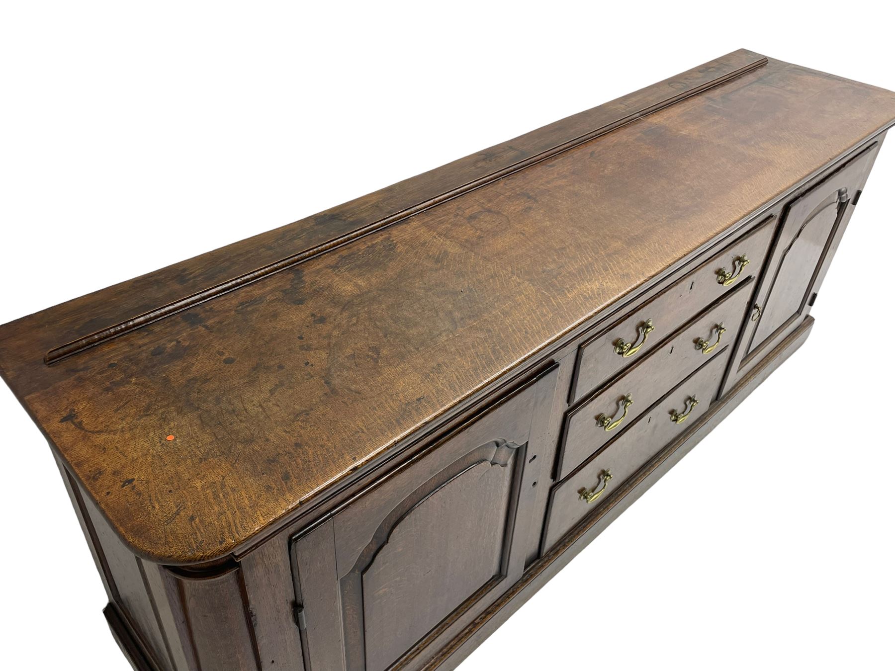 George III oak dresser base, rectangular top with rounded corners over moulded frieze rail, canted corners with turned quarter columns, fitted with three drawers with moulded edges flanked by two cupboards, enclosed by ogee arched fielded panelled doors, panelled sides, moulded plinth base