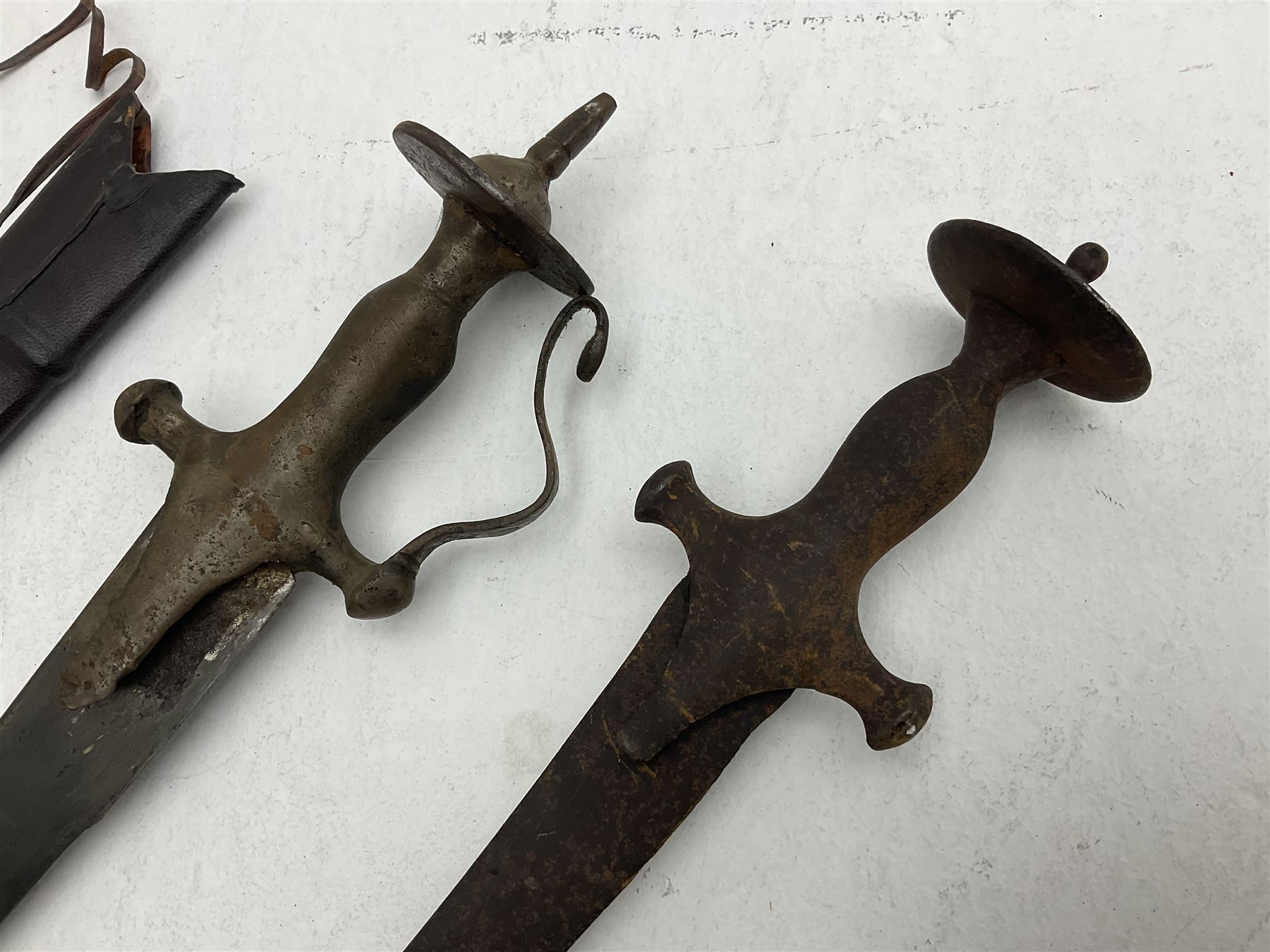 Late 19th/early 20th century Indian Tulwar sword with 81cm plain curving steel blade and iron hilt with extended langets, knucklebow and spiked pommel; in leather covered scabbard L100cm overall; and another Tulwar lacking scabbard in almost relic condition (2)