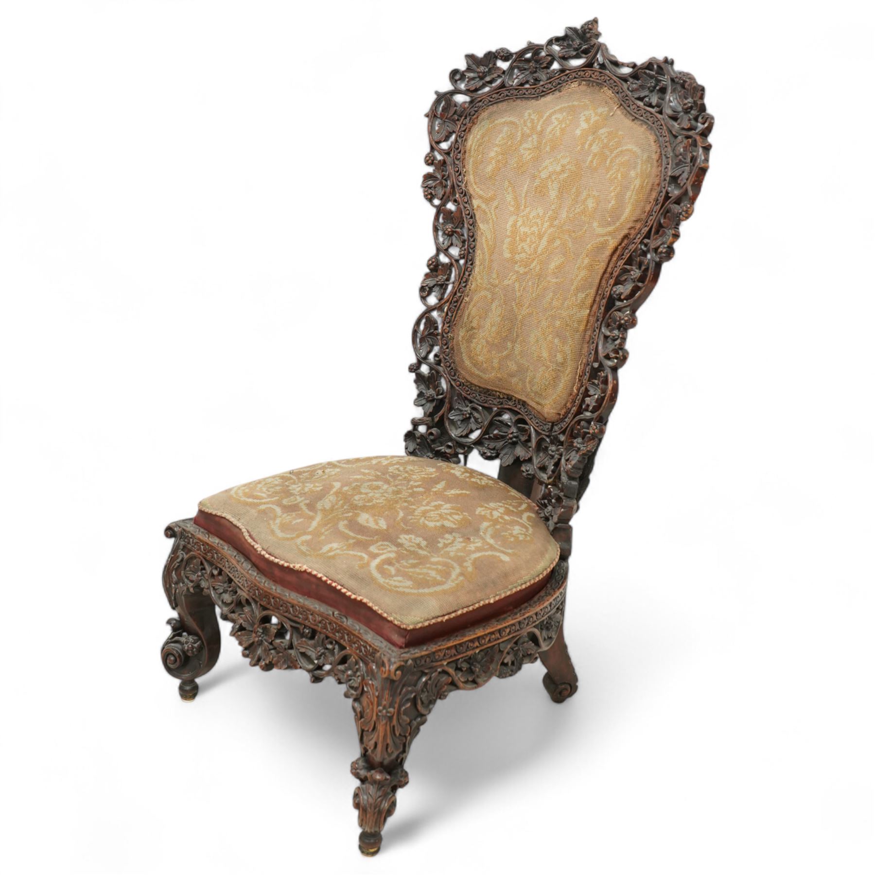 Late 19th century Anglo-Indian carved hardwood nursing chair, cartouche-shaped back, pierced fruit vine carved frame, gros-point tapestry upholstered seat, on carved scroll legs 