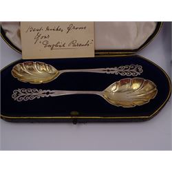 Set of eight modern silver place card holders, of pierced scrolling design, hallmarked Albert Edward Jones, Birmingham 1991, together with a pair of Edwardian silver preserve spoons, with fluted bowls and pierced scrolling handles, hallmarked Elkington & Co Ltd, Birmingham 1908, both contained within fitted silk and velvet lined fitted cases