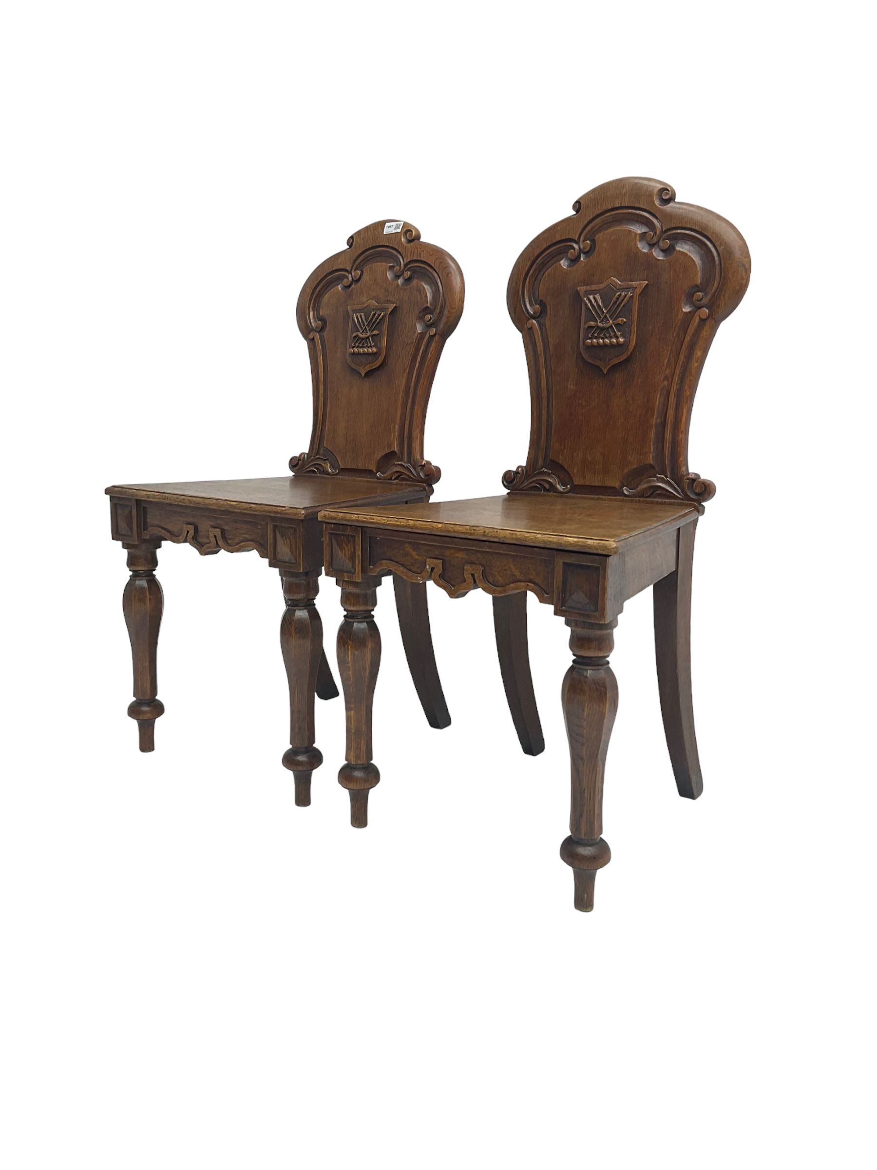 Pair Victorian oak hall chairs, scallop shaped back with carved scrolls and central shield moulding, panel seat over shaped frieze rail, raised on turned supports