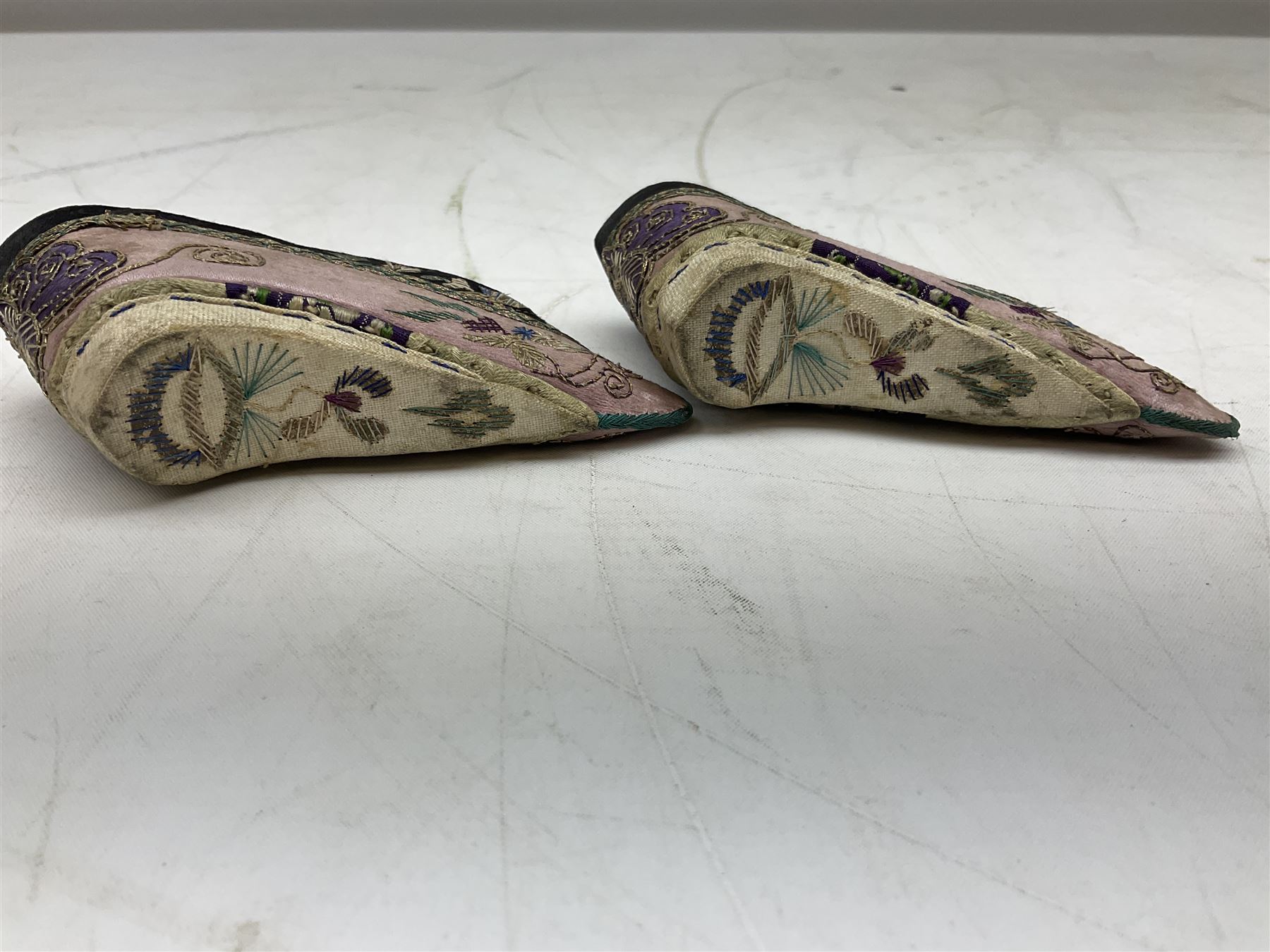 French silver plated wine taster of typical form, stamped, together with a silver plated napkin ring, and an 'Alpaca Silver' pill box with mother of pearl detailed cover, (3) together with Two pairs of late 19th/early 20th century Chinese Lotus shoes for binding feet, the first with purple silk heavily embroidered with ornate floral motifs, L10cm the second larger fuschia and black pair with thicker sole embroidered with flowers, L14cm