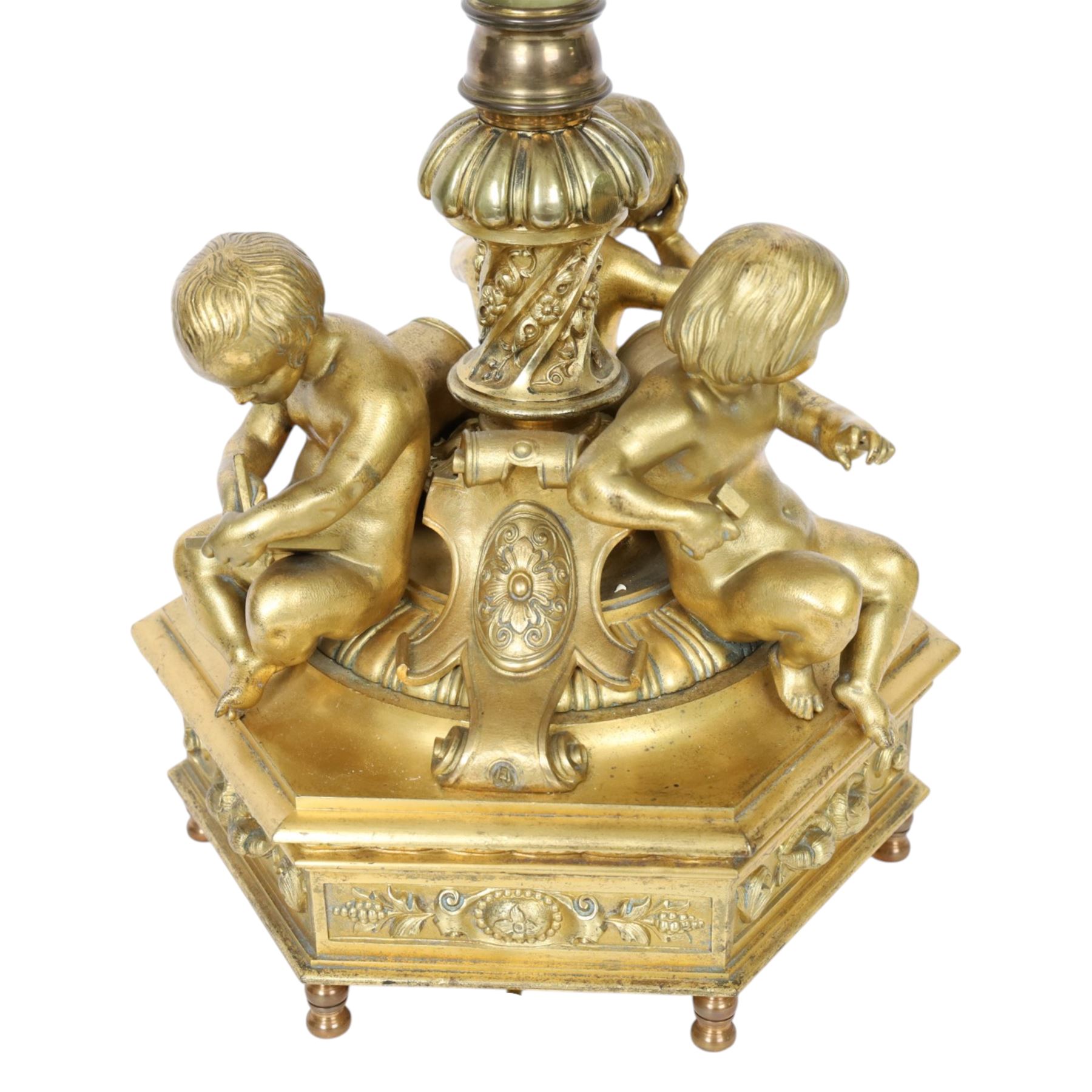 Second Empire style gilt metal table lamp, the hexagonal plinth base with applied foliate decoration, upon six turned feet, supporting three seated allegorical putti, the first modelled with a tablet and stylus representing literature, the second with hammer representing sculpture, and the third with Corinthian column capital representing Architecture, each intersected by a stylised scroll with central flower head panel, mounted upon an onyx and gilt metal Corinthian column with wrythen flower moulded and part fluted base, supporting a cream octagonal shade, overall H86cm