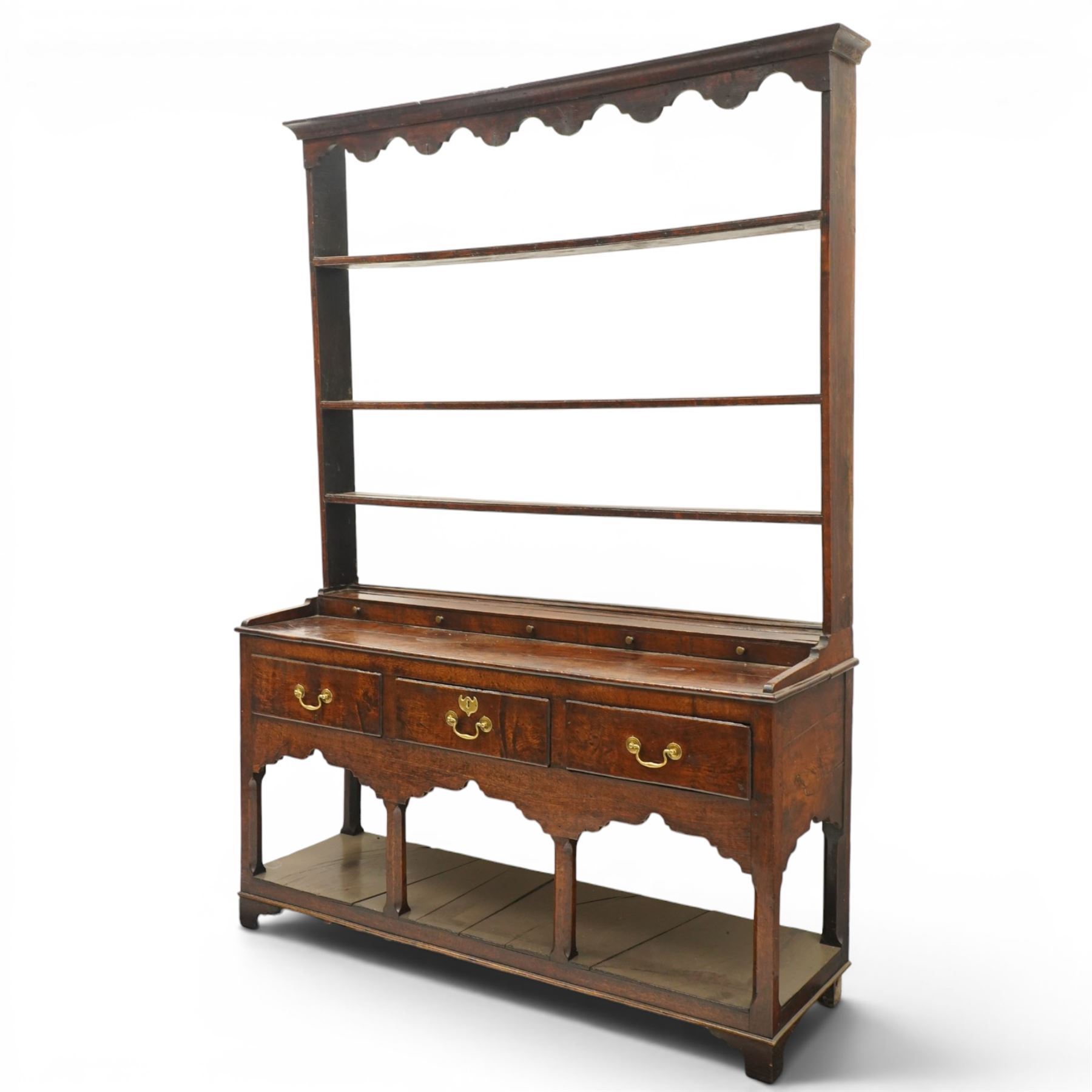 18th century Georgian oak dresser base with plate rack, the three-tier plate rack with shaped frieze, the base with rectangular top with raised back fitted with five spice drawers, over three drawers with brass swan neck handles, raised on six square chamfered supports united by undertier 