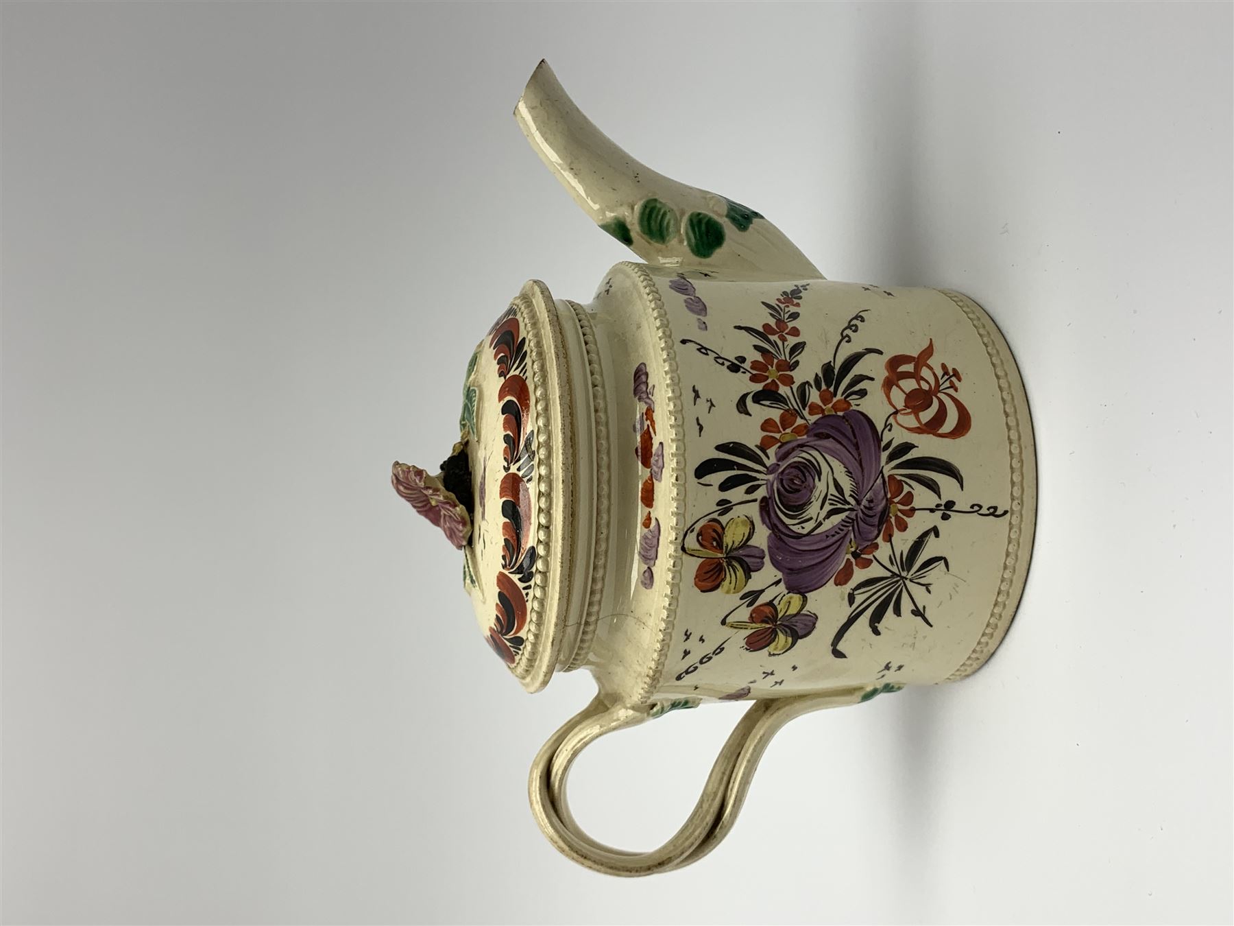 18th century creamware teapot, probably Leeds, with reeded entwined handle and floral finial to the cover, the body with hand painted polychrome decoration of figure to one side, and floral spray to the other, collectors paper label beneath inscribed Leeds Pottery, H11.5cm