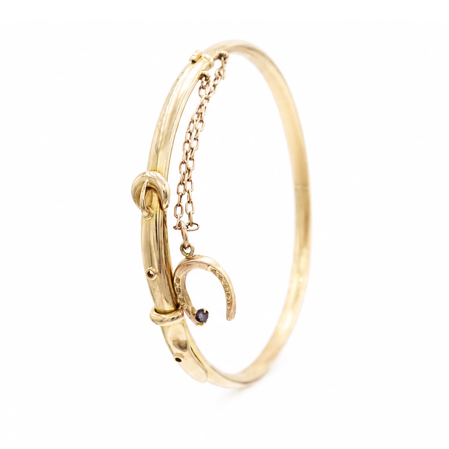 Early 20th century 15ct gold buckle hinged bangle, stamped 15, the safety chain with a 9ct rose gold horseshoe charm, set with a single sapphire