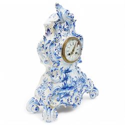 19th century delft blue and white Rococo style 8-day mantle clock, with a scrolling case and floral decoration, depiction of a courting couple in 18th century dress to the front and a contrasting scene of sailing ships on a lake to the rear, with a late 19th-century French twin train movement, enamel dial with Roman numerals, five minute Arabic's and gilt Louis XVI hands within a glazed cast bezel, with a rack striking movement sounding the hours and half-hours on a bell. No pendulum or key.  