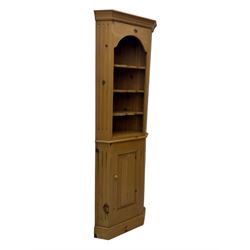 Early 20th century pine corner cabinet, projecting cornice over three shaped shelves, base fitted with single door enclosing storage space with a recessed panel, fluted sides, on plinth base
