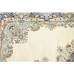 South East Persian Kirman hand-knotted carpet, ivory field with central floral medallion in tones of cobalt and pale blue, issuing scrolling vinery and palmettes, conforming spandrels, main border with scrolling foliage and stylized palmettes, framed by multiple guard borders, with cotton fringe ends 