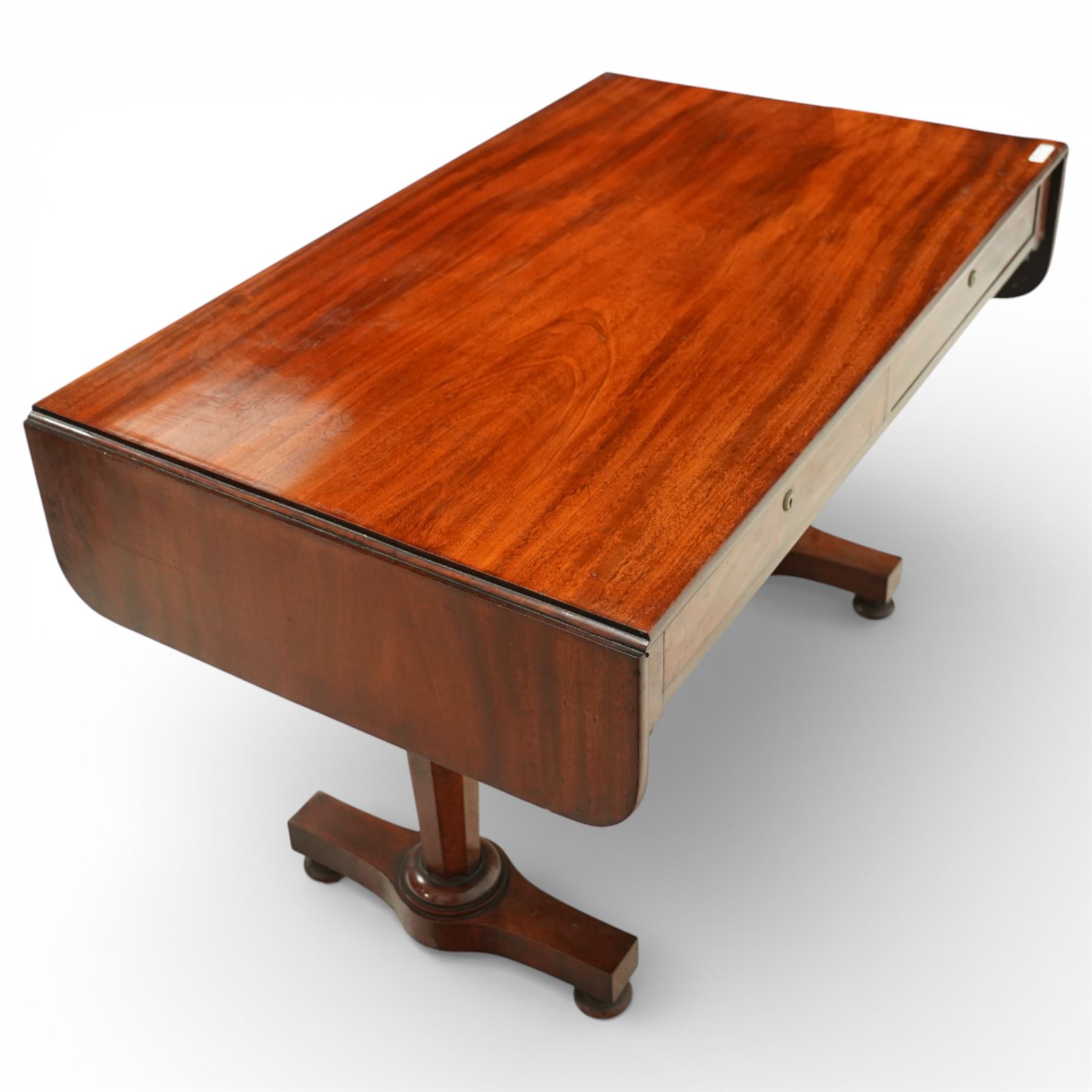 William IV mahogany sofa table, the rectangular top with rounded corners and hinged drop leaves to either end, above a shallow frieze fitted with two drawers opposing conforming dummy drawers, supported on octagonal tapering legs with ring turnings, joined by a shaped stretcher and raised on platform bases with scroll feet