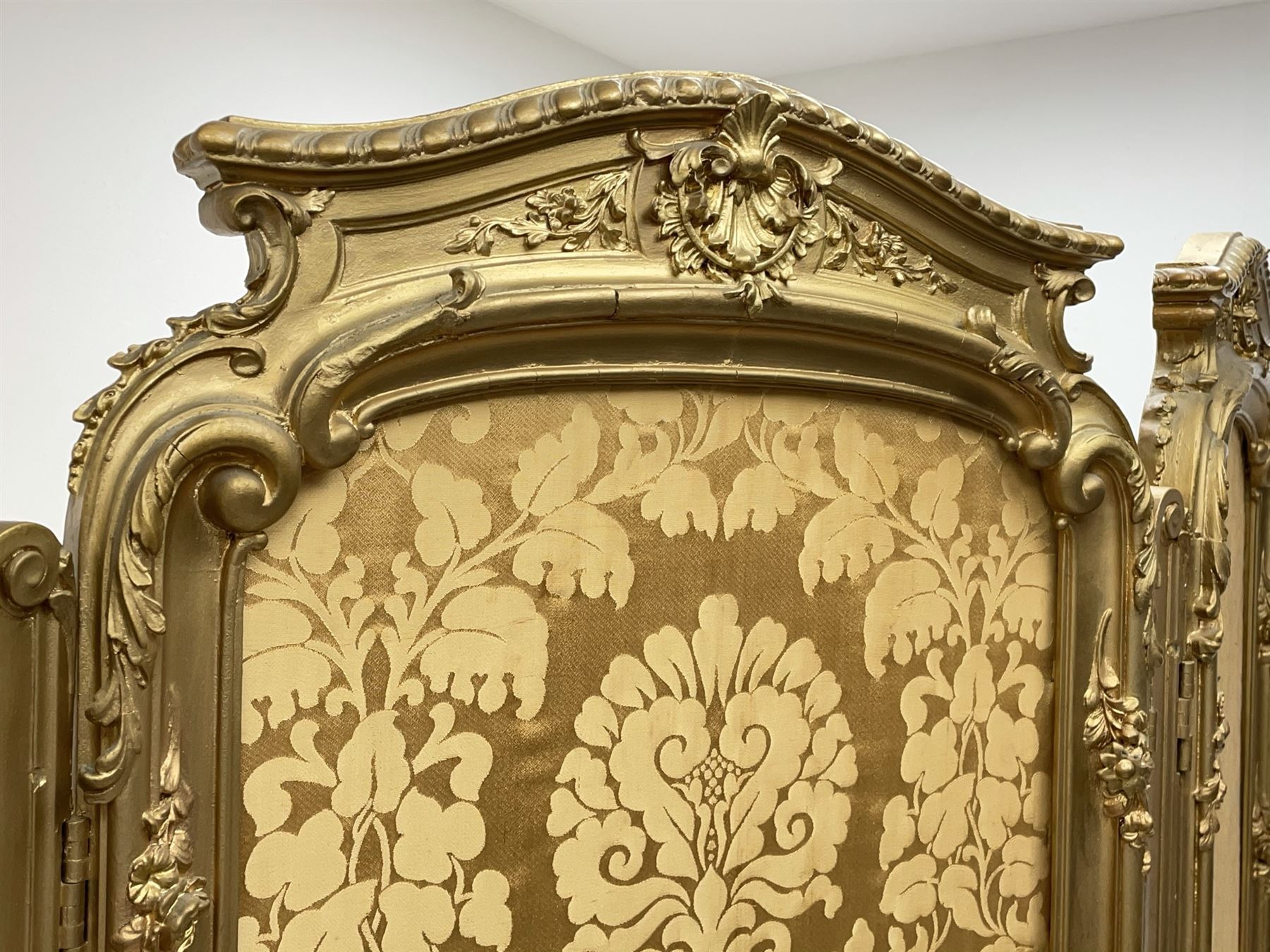 Late 19th/early 20th century French Rococo style gilt wood and gesso dressing screen, four double hinged panels, each with shaped cresting rail over shell and floral frieze, moulded frame with flower head and scroll decoration, acanthus leaf cabriole supports with castors, upholstered in gold Damask fabric