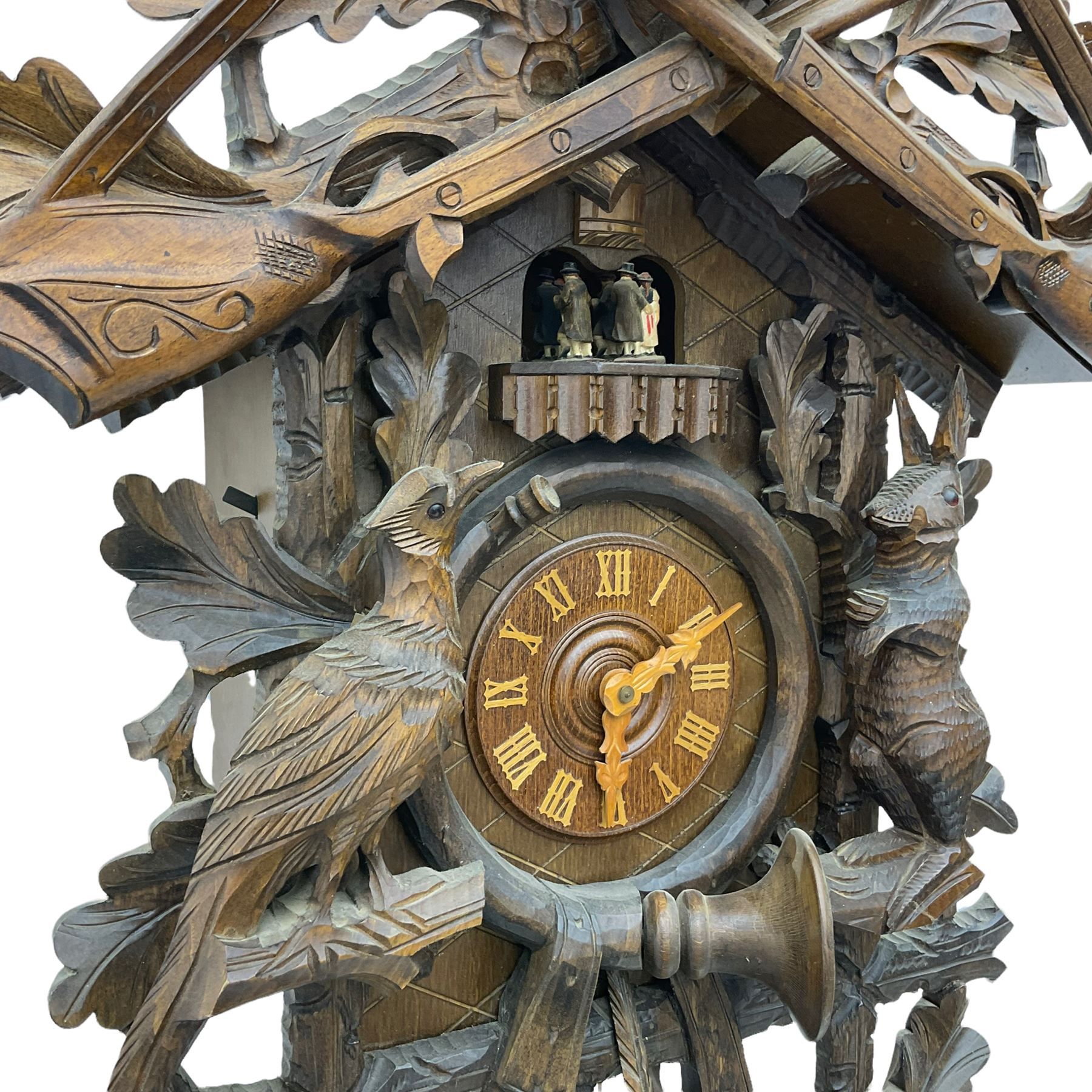 A large and imposing 20th century three train 30hr cuckoo clock with automata and musical features, profusely carved case with a carousel, animals, leaves and sporting guns, dial with pierced wooden numerals and wooden hands, with three weights and pendulum, strike/silent facility. 
