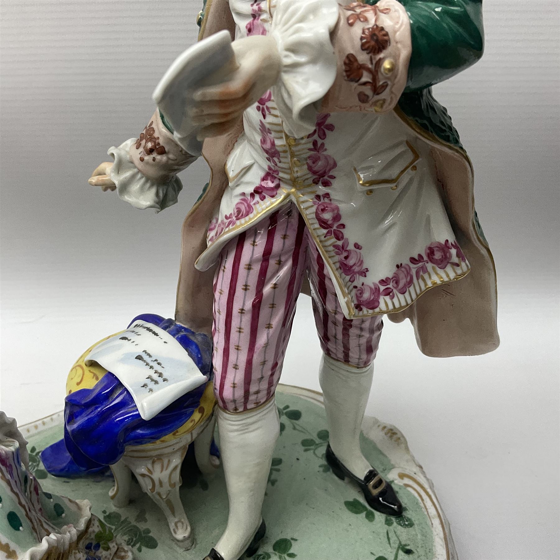 20th century Naples figure group, modelled as a seated female figure playing the lute seated, before a male figure stood holding a sheet of music, each in period dress, upon an oval base with gilt heightened scroll edge, with crowned N mark beneath, H31.5cm L33cm
