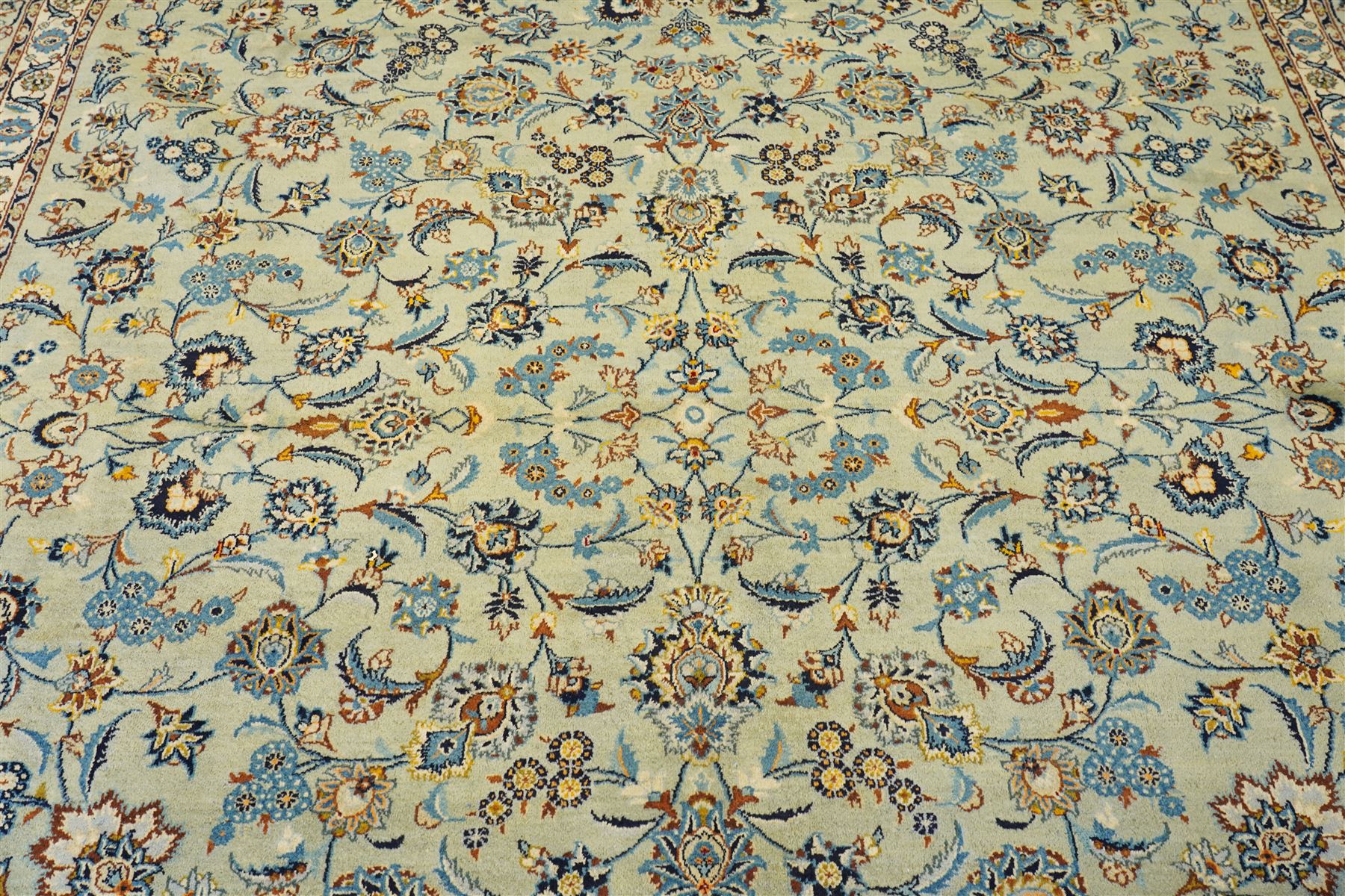 Central Persian Kashan hand-knotted carpet, pale blue field decorated with an all-over scrolling floral vine design incorporating stylized palmettes, rosettes and foliate sprays enclosed by a conforming floral vine border between multiple guard stripes, with cotton fringe ends 