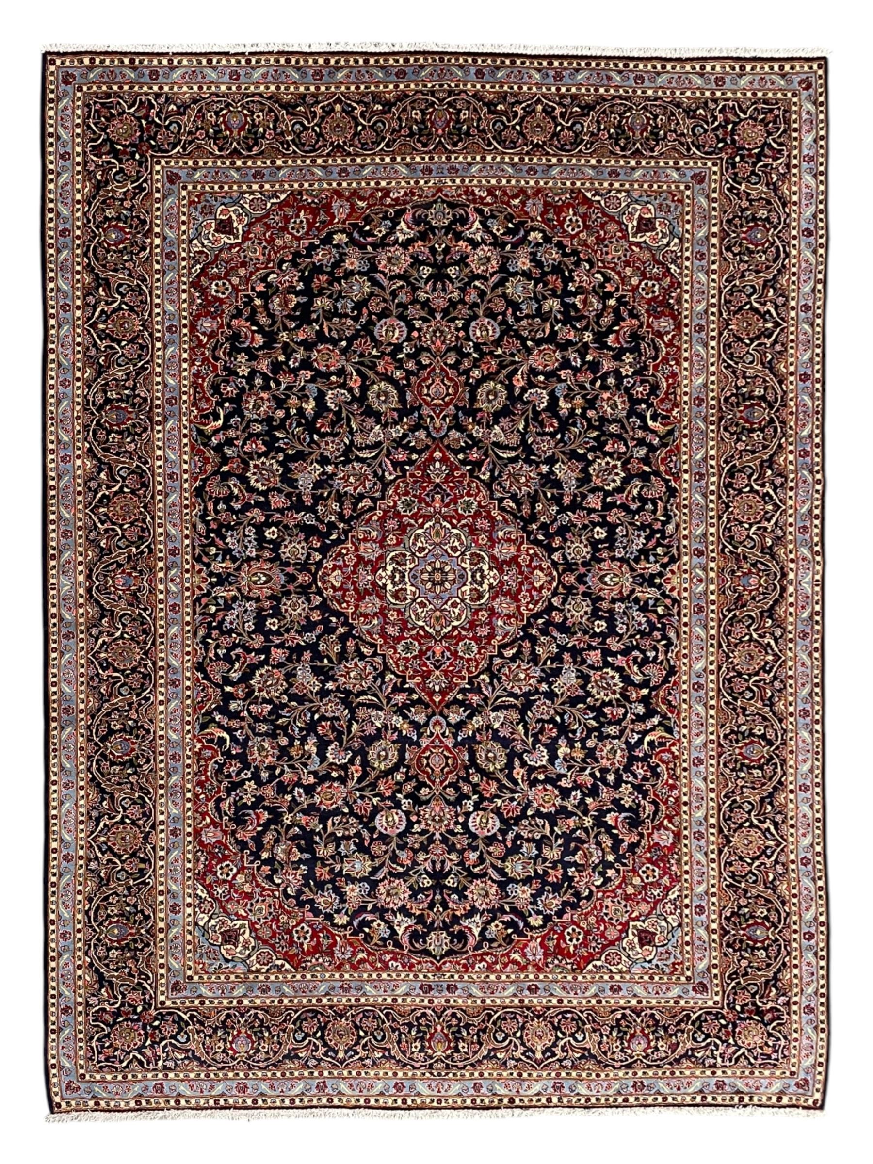 Persian Kashan indigo ground carpet, central floral pattern medallion surrounded by a densely decorated field depicting trailing branches with leaves and palmettes, scrolling border decorated with stylised plant motifs, within floral pattern guard stripes 