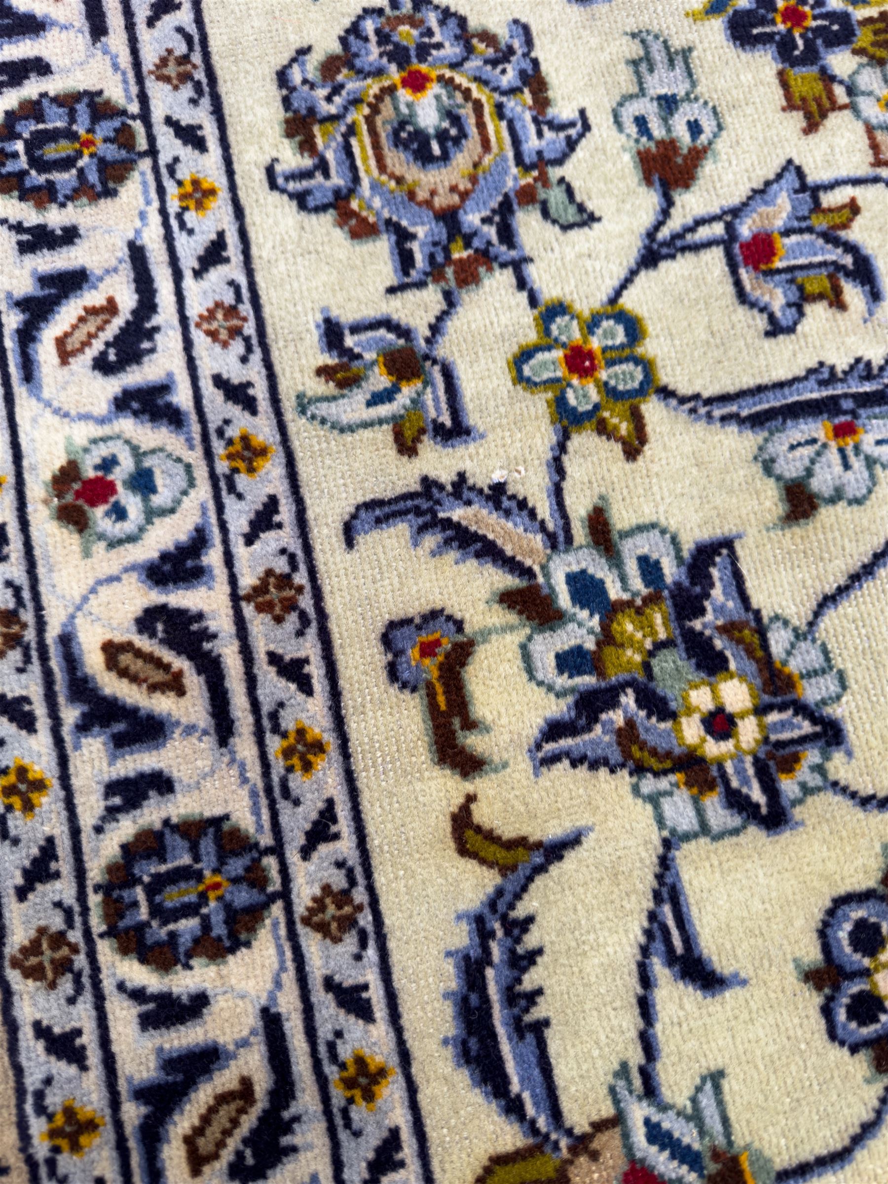 Central Persian Kashan hand-knotted carpet, ivory field with an all-over design of scrolling vines, lotus palmettes, and rosettes in shades of blue, gold, and brown within a blue ground border of palmettes and arabesques between multiple guard stripes