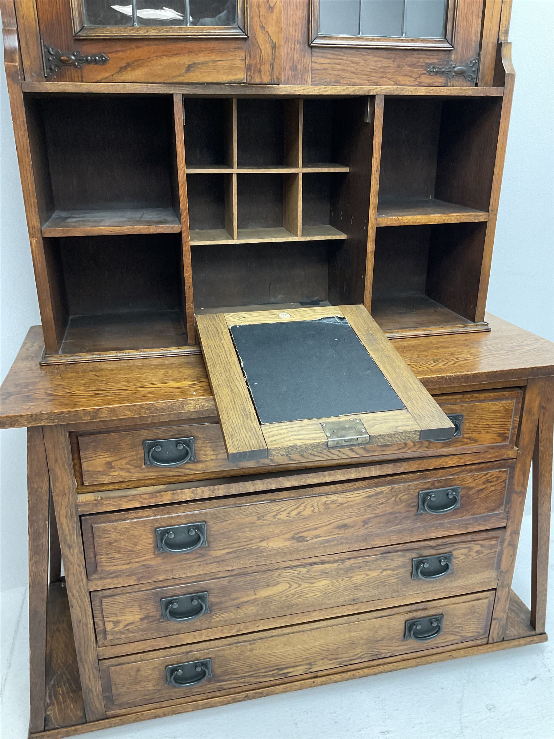 Arts & Crafts oak cabinet on chest, projecting cornice above to lead glazed cabinet doors, two shelves flanking single fall front enclosing fitted interior, four graduating drawers