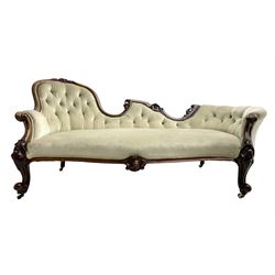 Victorian walnut chaise longue or settee, shaped back carved with cartouche motifs and foliage, upholstered in buttoned pale fabric with sprung seat, scrolled arm terminals on shaped supports with cartouche carved knees, cabriole feet on brass and ceramic castors 
