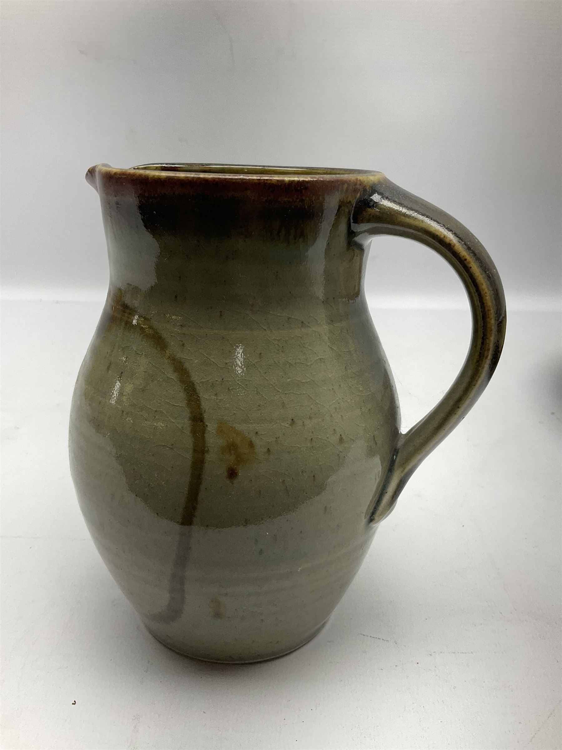 Michael Leach (British 1913-1985) for Yelland pottery; two large glazed stoneware plates with dark brown stylised decoration upon oatmeal ground, together with a jug in merging blue, green and brown, all with impressed marks beneath, largest plate D37cm