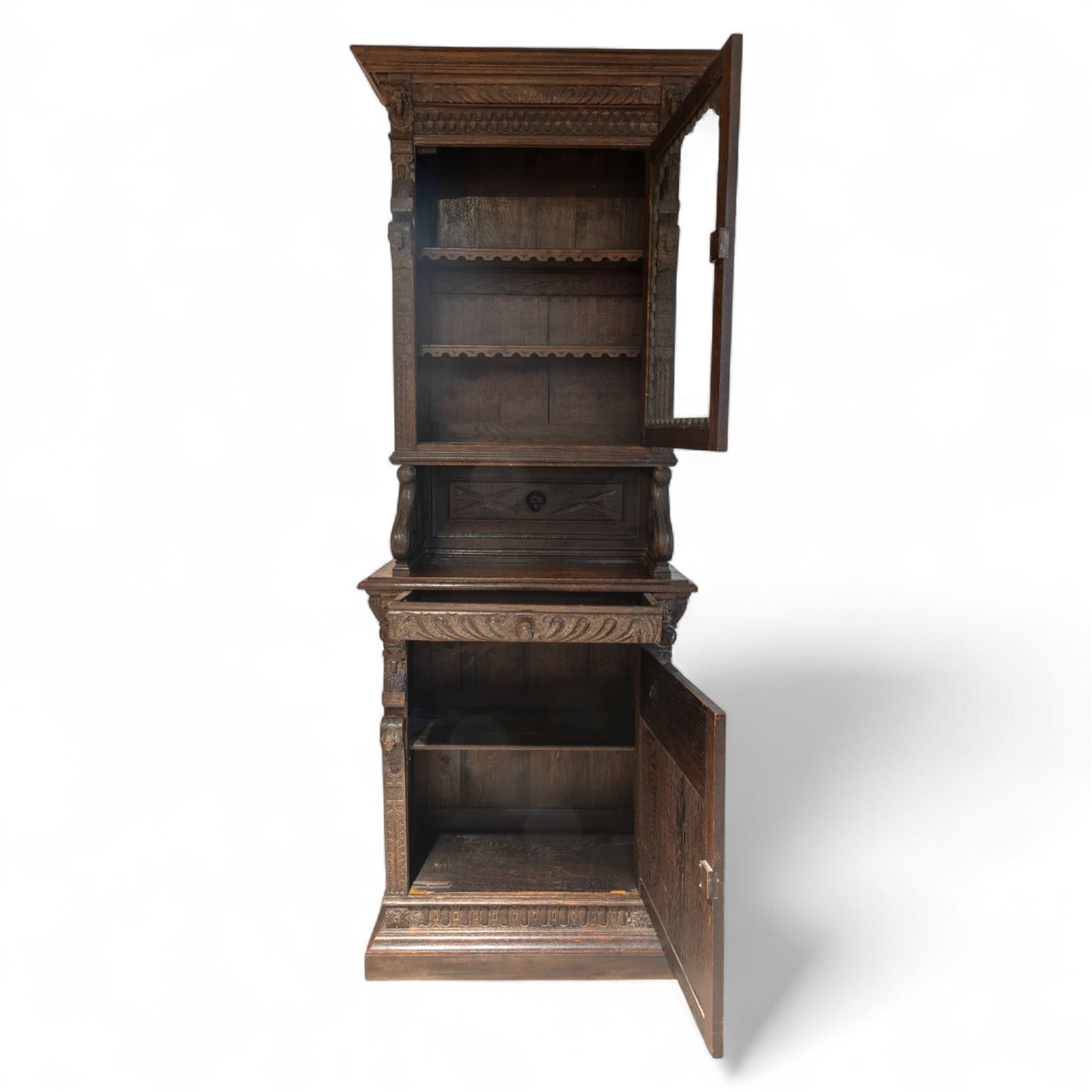 French carved oak cabinet in the Renaissance revival style, cornice carved with scrolling acanthus flanked by lion mask ring terminals, above glazed door with scroll supports over a carved panelled cupboard section with radiating shell motif and geometric quarter panels with foliate ornamentation, raised on a moulded plinth base 