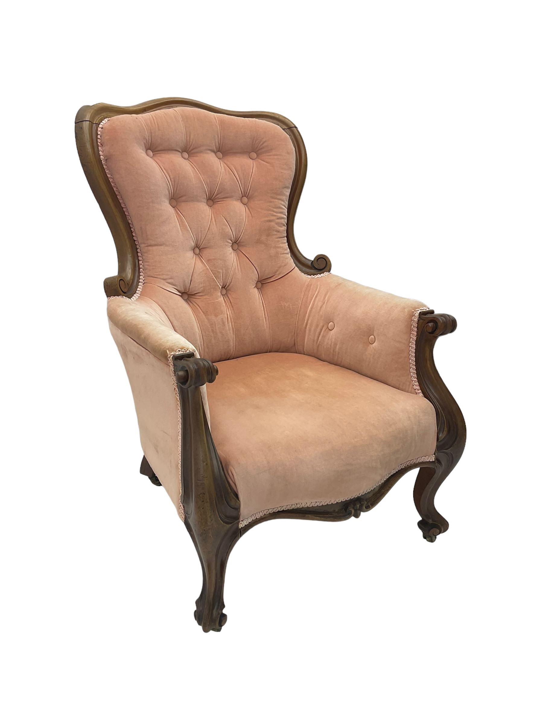 Victorian walnut framed armchair, shaped back with carved and scrolled arm terminals, upholstered in buttoned pale pink fabric, raised on cabriole supports terminating in castors