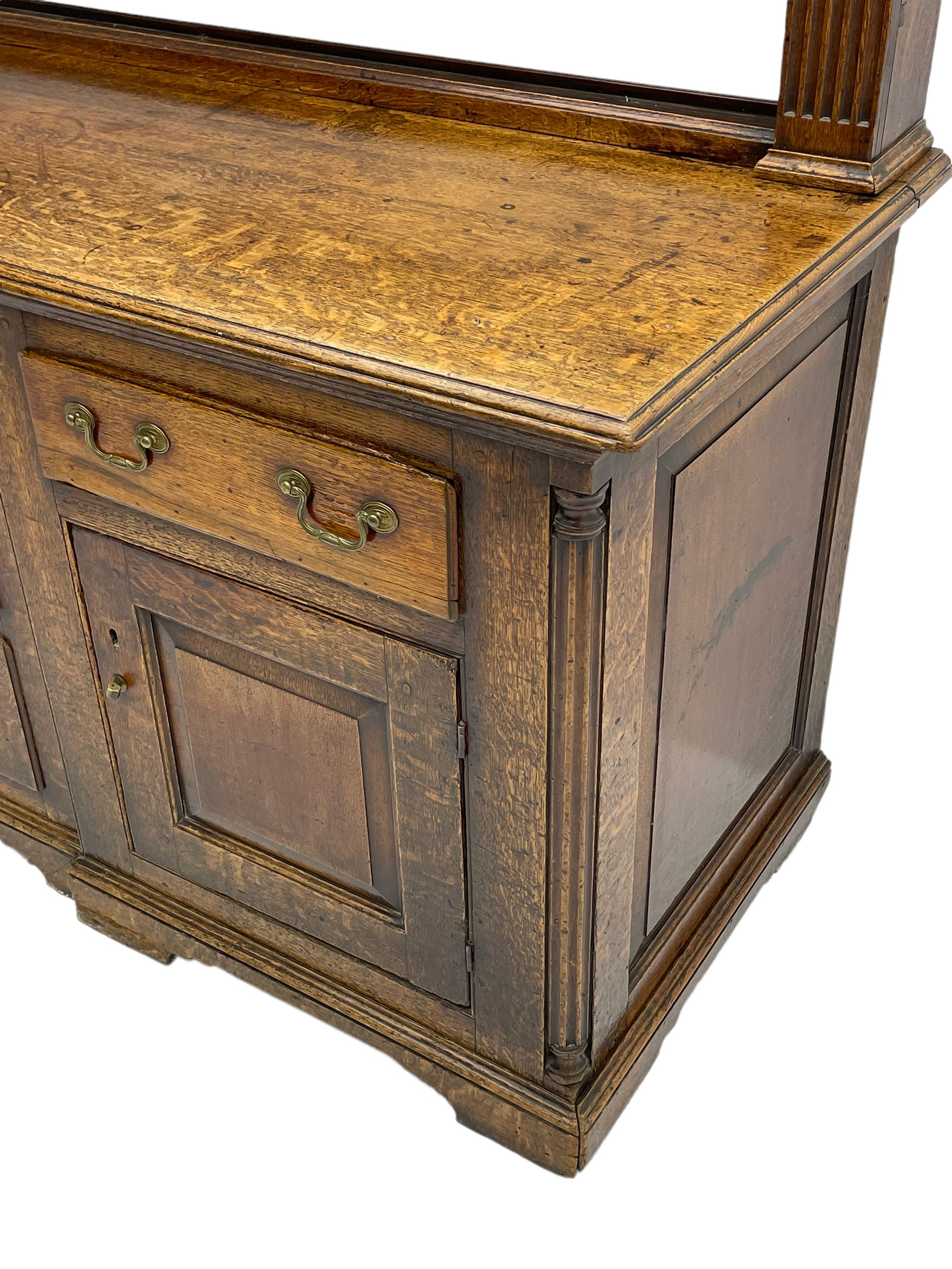 George III oak dresser, projecting dentil cornice over three heights plate rack enclosed by fluted uprights, the dresser fitted with five drawers and two panelled cupboards, canted corners with fluted quarter columns, on bracket feet