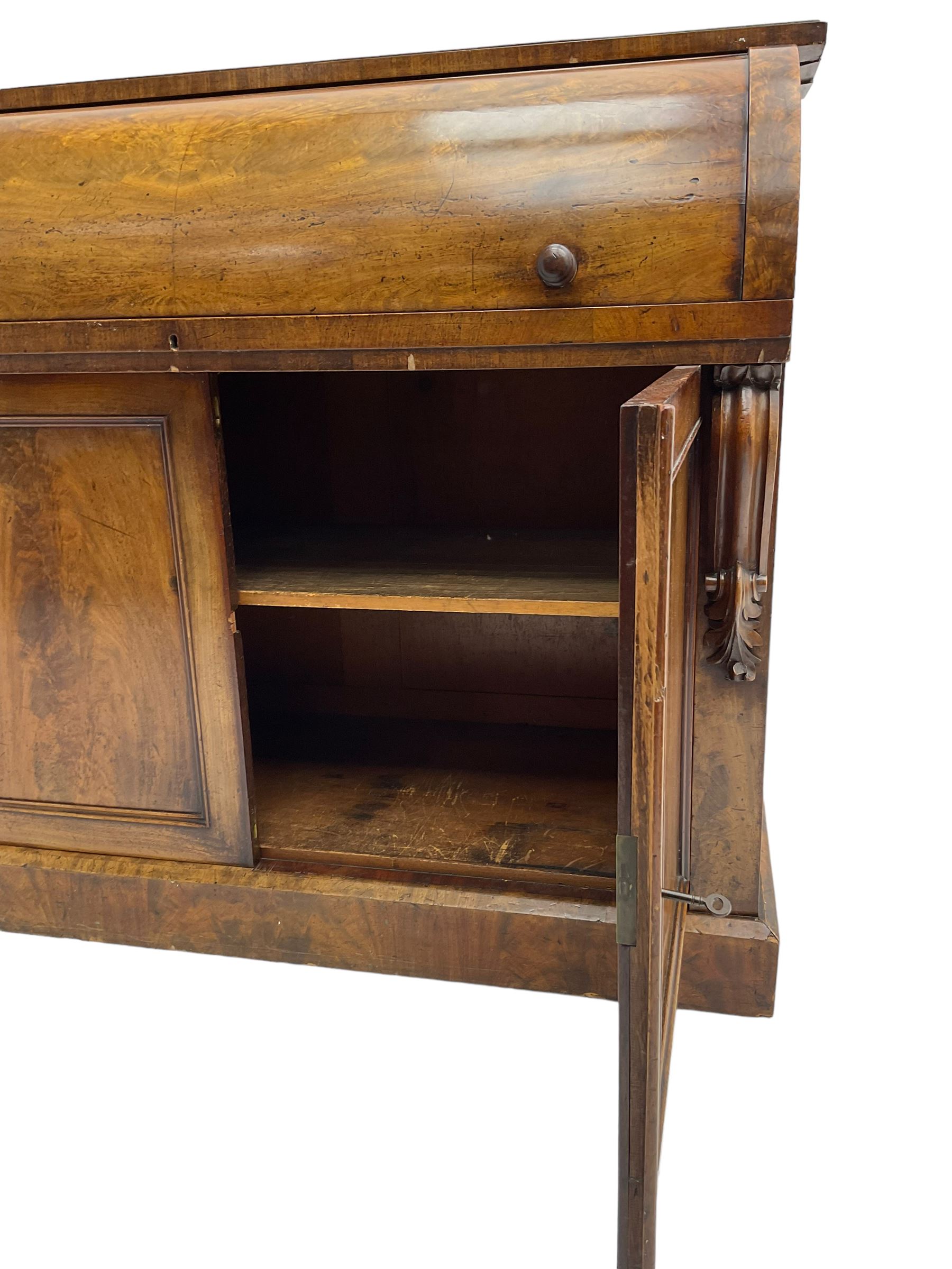 Victorian mahogany roll-top writing desk, top concealing fitted interior with pigeonholes and three drawers, the trisector inset writing surface with writing slope, base fitted with panelled cupboard enclosing single shelf, decorated with scrolled corbels