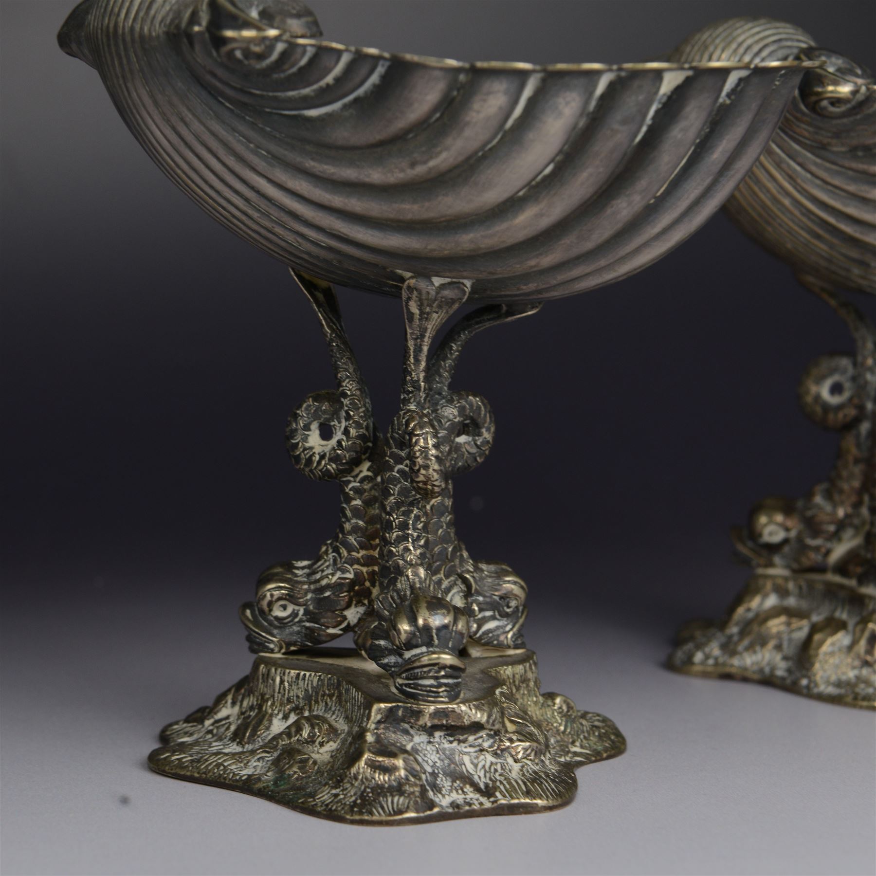 Pair of Victorian silver plated comports, with clam shell bowls supported by three dolphins upon a rocky base, H12cm