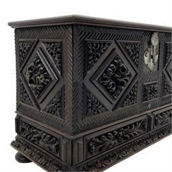 Early 20th century carved hardwood kist or mule chest of small proportions, moulded rectangular hinged lid over foliage carved geometric lozenge panels, the frame carved with chevron banding, fitted with two drawers, the drawer fronts carved with extending leaf motifs over a foliage carved lower moulding, on turned feet