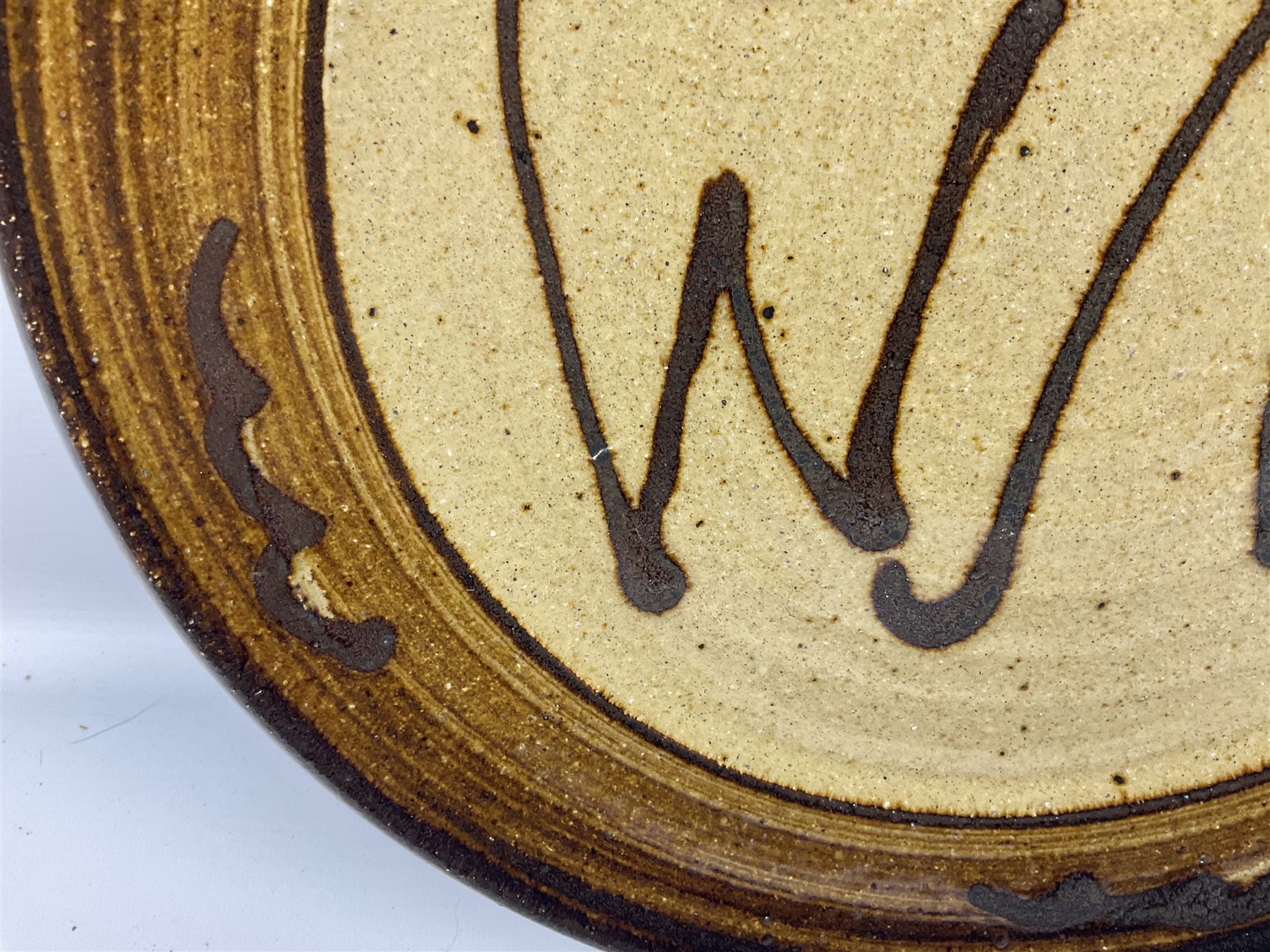 Michael Leach (British 1913-1985) for Yelland pottery; two large glazed stoneware plates with dark brown stylised decoration upon oatmeal ground, together with a jug in merging blue, green and brown, all with impressed marks beneath, largest plate D37cm