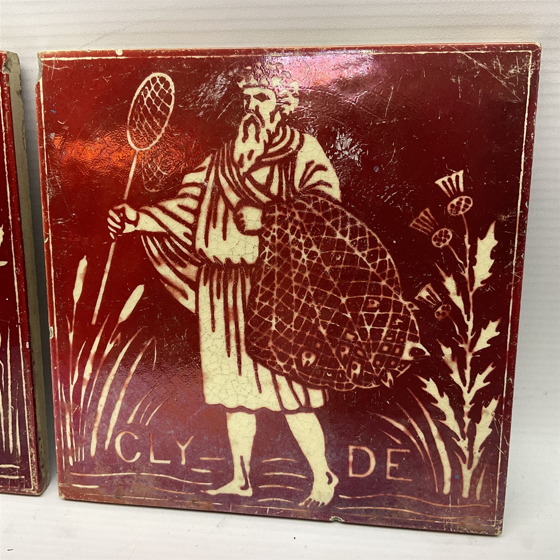 Pair of Maw & Co Benthall Works tiles, each depicting classical figures with fishing and shipping details, one inscribed Thames, the other Clyde, upon a red lustre ground, with raised marks verso, H15.2cm