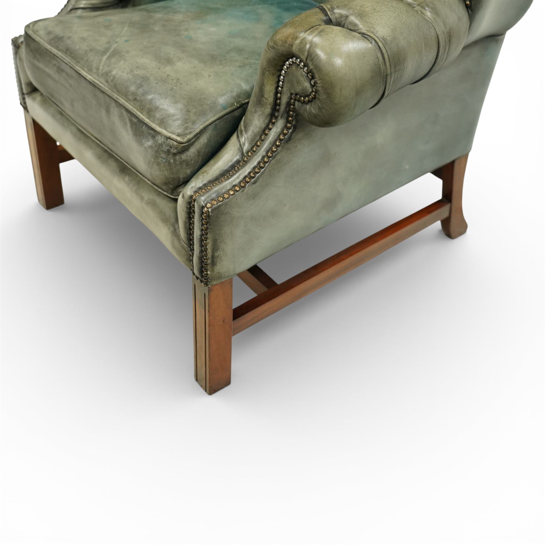 Georgian design mahogany framed wingback armchair, upholstered in rustic pale green buttoned leather with loose seat cushion, raised on square supports united by H-stretcher