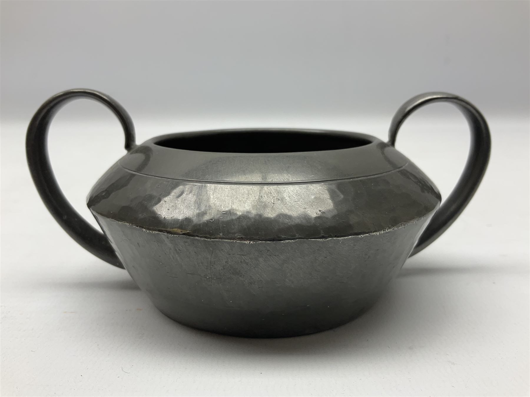 Liberty & Co Tudric pewter three piece tea service, comprising teapot with woven reed handle, twin handled open sucrier, and milk jug, each of squat form with planished finish, each impressed beneath Tudric Pewter Ware 01537 Made in England, together with a matched unmarked tray