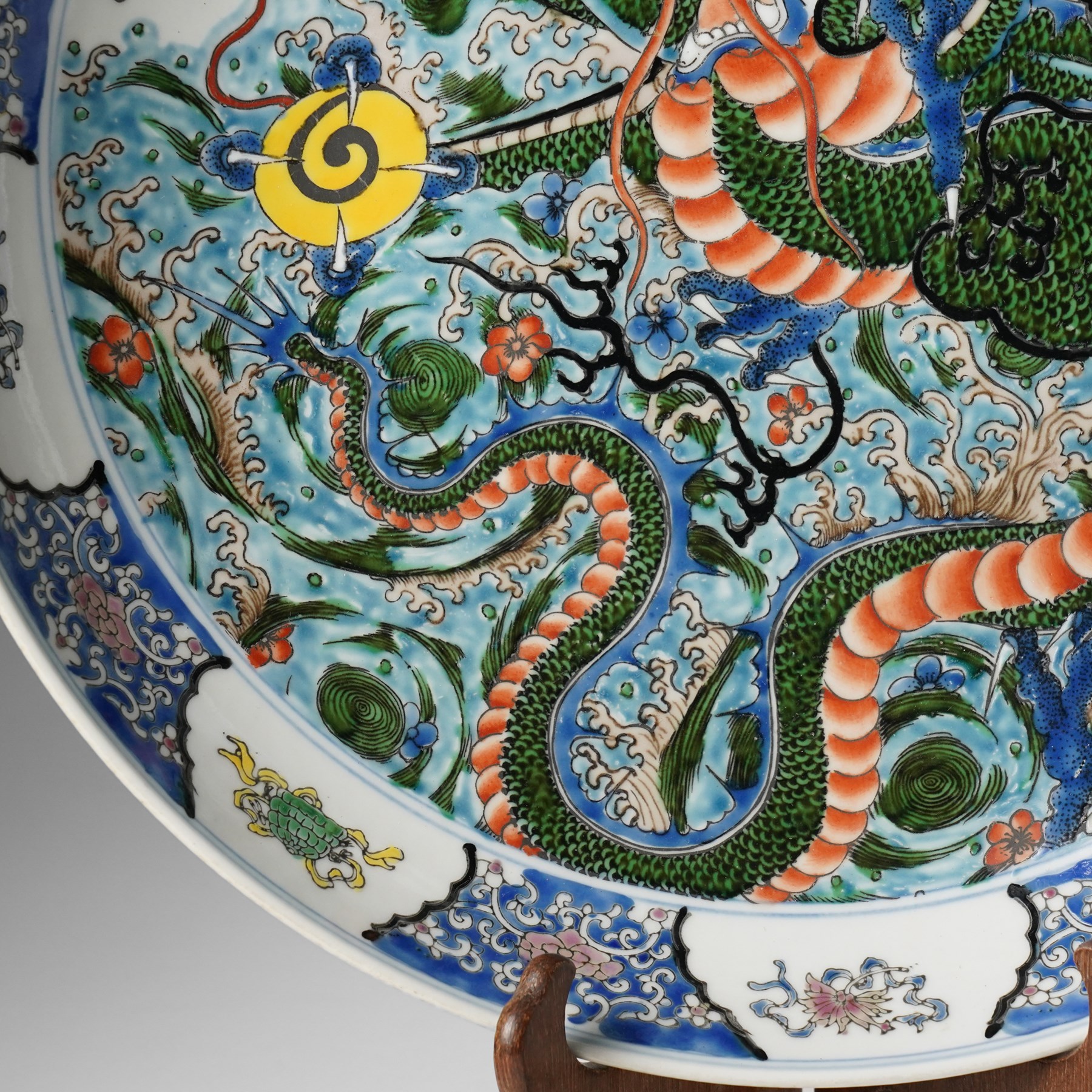 Chinese charger, decorated in blue, green and red enamels with a four clawed dragon chasing the flaming pearl amidst waves and flower heads, the rim with border of alternating reserves of auspicious emblems and flower scrolls, bearing apocryphal Kangxi mark beneath, D38cm 

