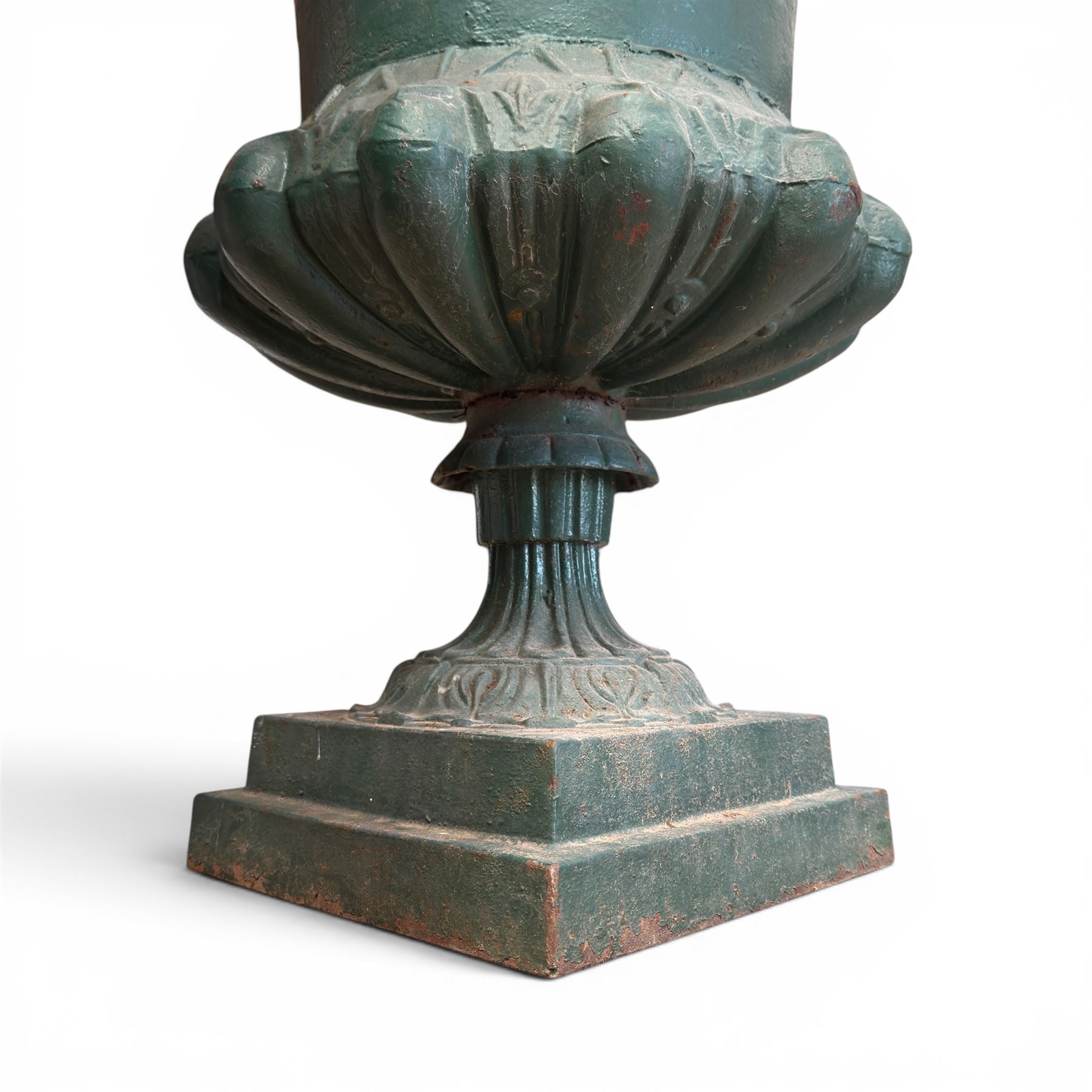 Pair of Victorian cast iron campana garden urns, the flared rim with repeating stylised anthemion motifs with scrollwork, over a deep gadrooned and Aesthetic moulded underbelly, fluted and foliate lower bowls on square pedestal bases, in antique green-painted finish