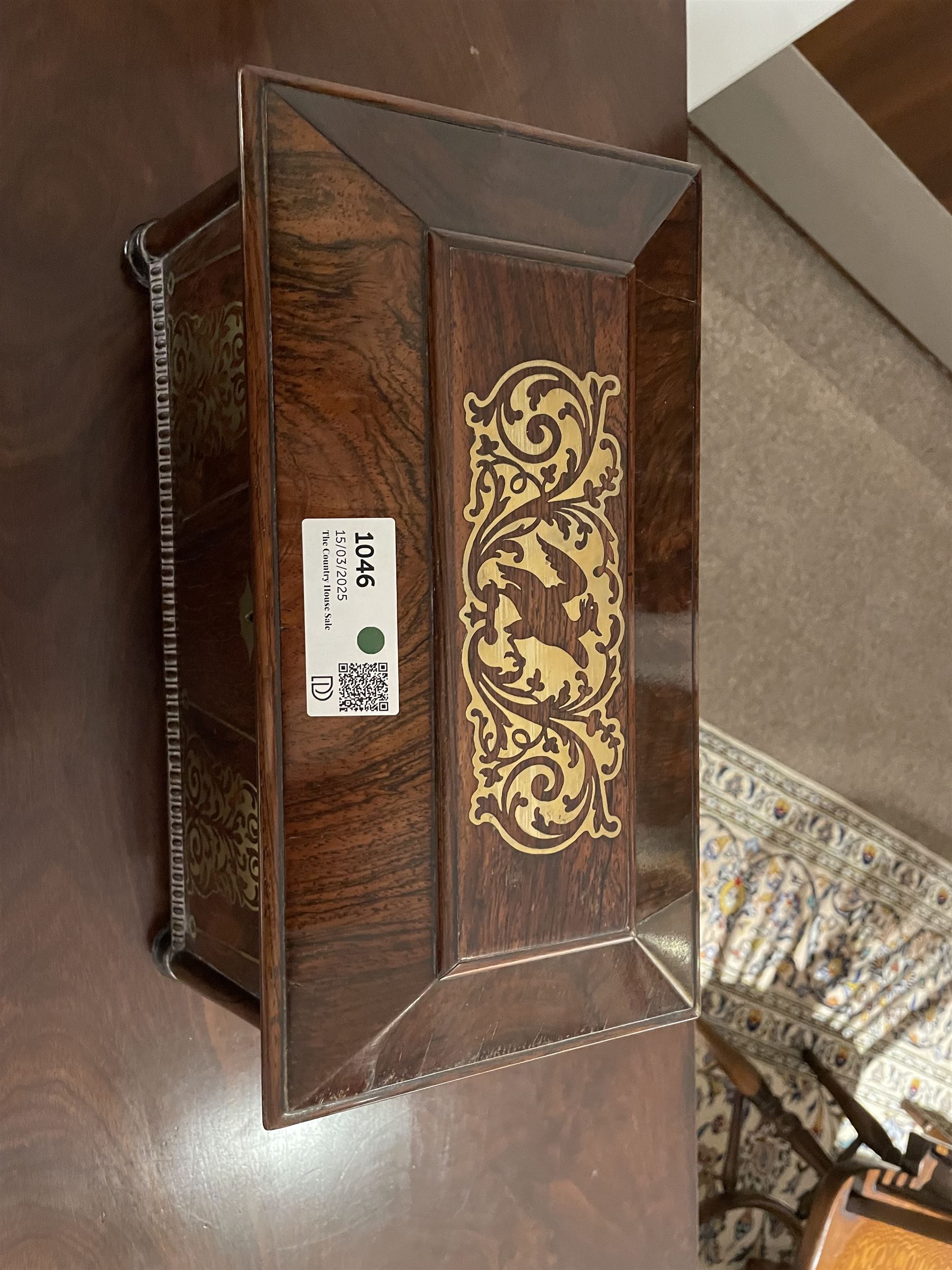 Early 19th century rosewood and brass inlaid tea caddy, of sarcophagus form, the front and hinged opening cover inlaid with brass scrolling panels, opening to reveal a compartmented interior with twin removable boxes with conforming inlaid brass detail to the hinged covers and zinc lining to the interiors, flanking a later glass mixing bowl, the whole upon four turned cylindrical feet, H21cm W36cm D20cm